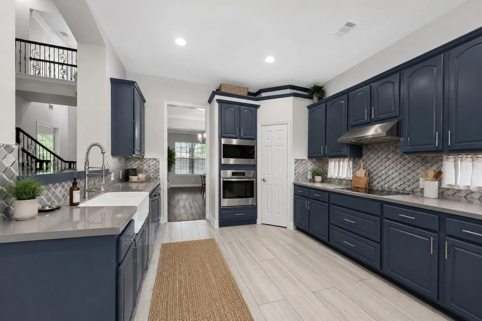 Dark blue cabinetry with stainless steel appliances, a farmhouse sink, and light wood-finish flooring