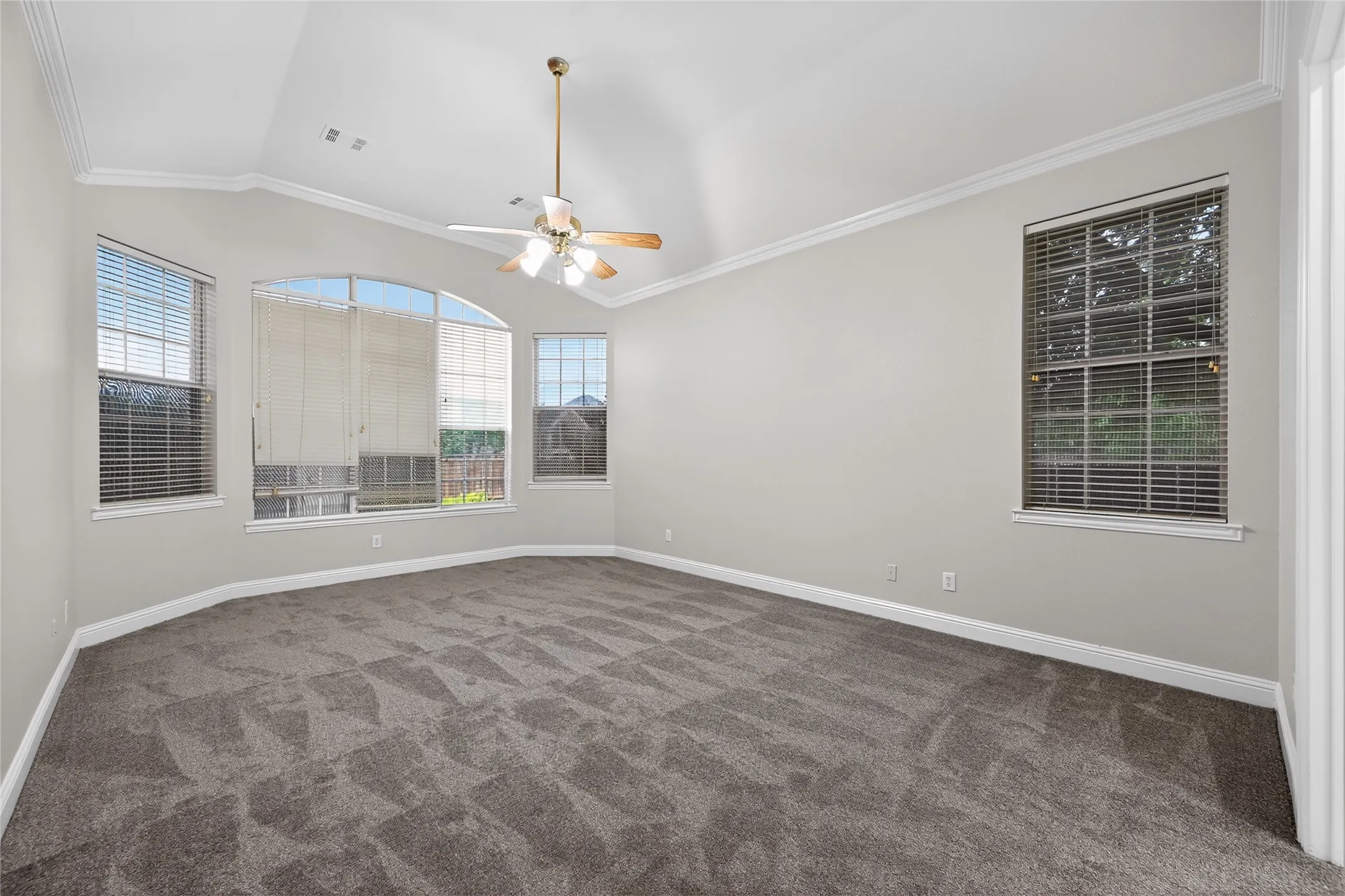 Spacious first floor primary bedroom room featuring a vaulted ceiling with crown molding, a ceiling fan with light fixture, and light gray wall paint