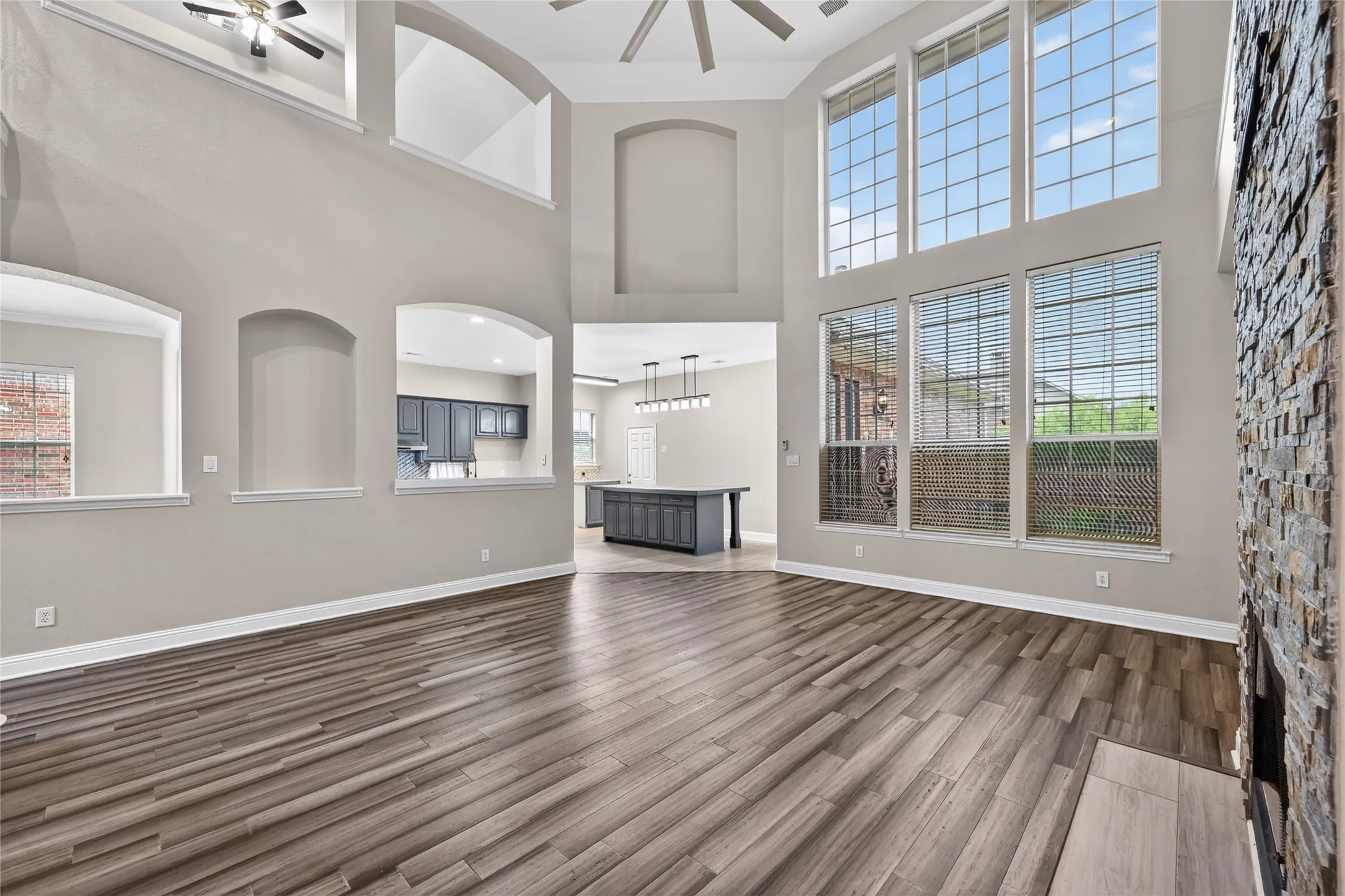 Two-story living area featuring wood-finish flooring, a stone-clad fireplace, and multiple tall windows