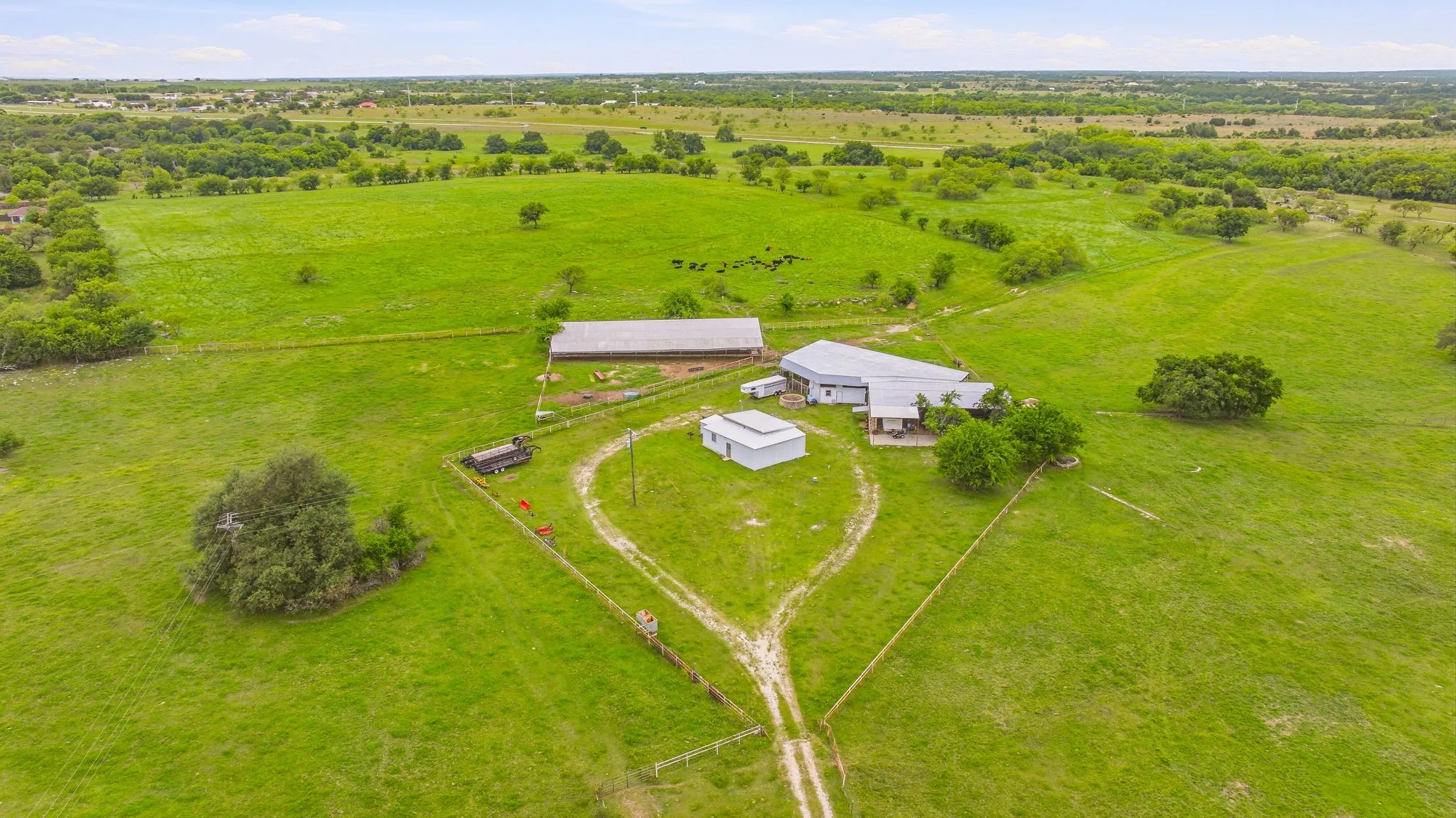 Expansive green acreage featuring a primary residence with an attached garage, a large barn, and a secondary outbuilding