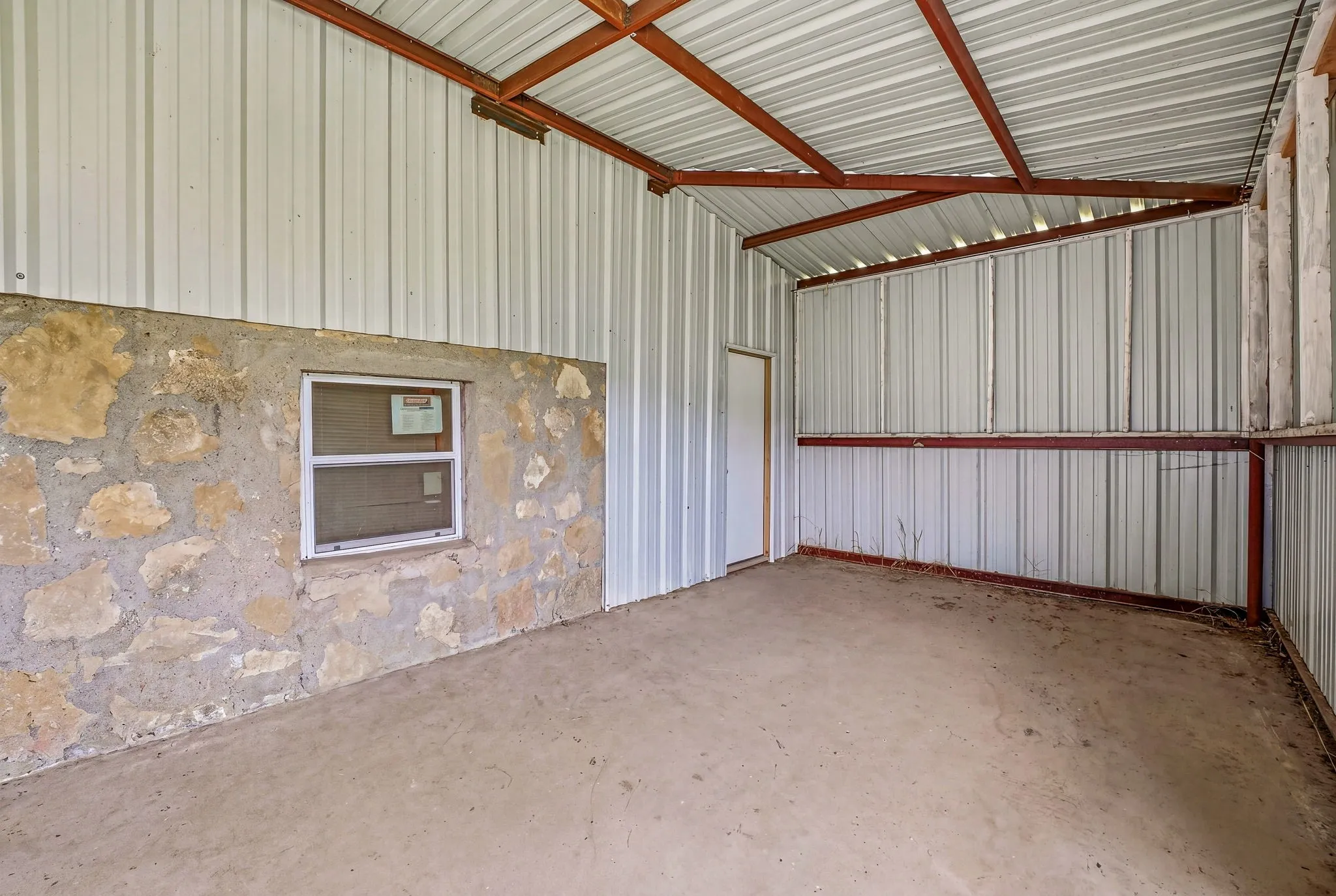 Covered structure featuring a concrete floor, metal siding, and exposed structural beams