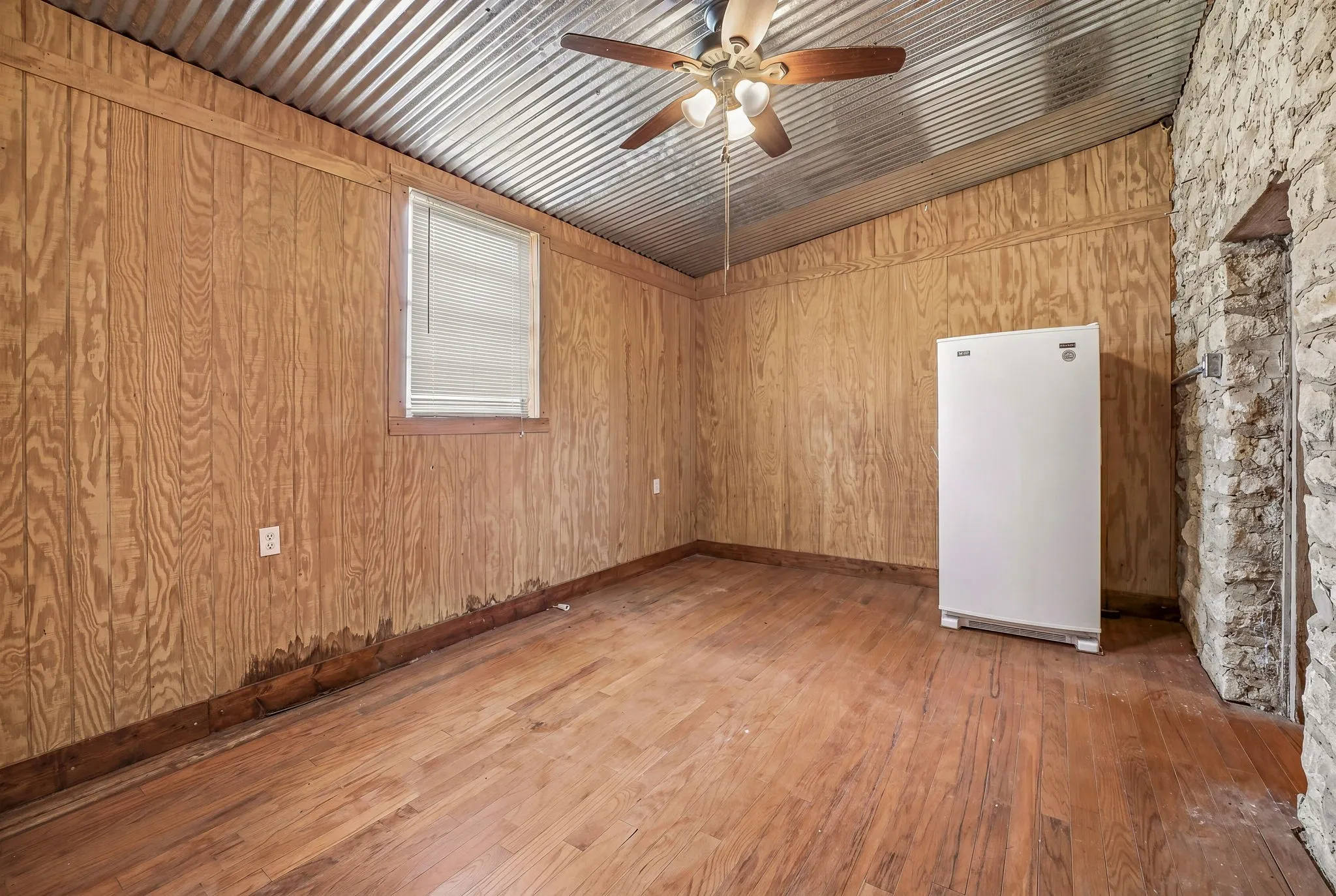 Room featuring wood-finish flooring, wood paneling, and a corrugated metal ceiling