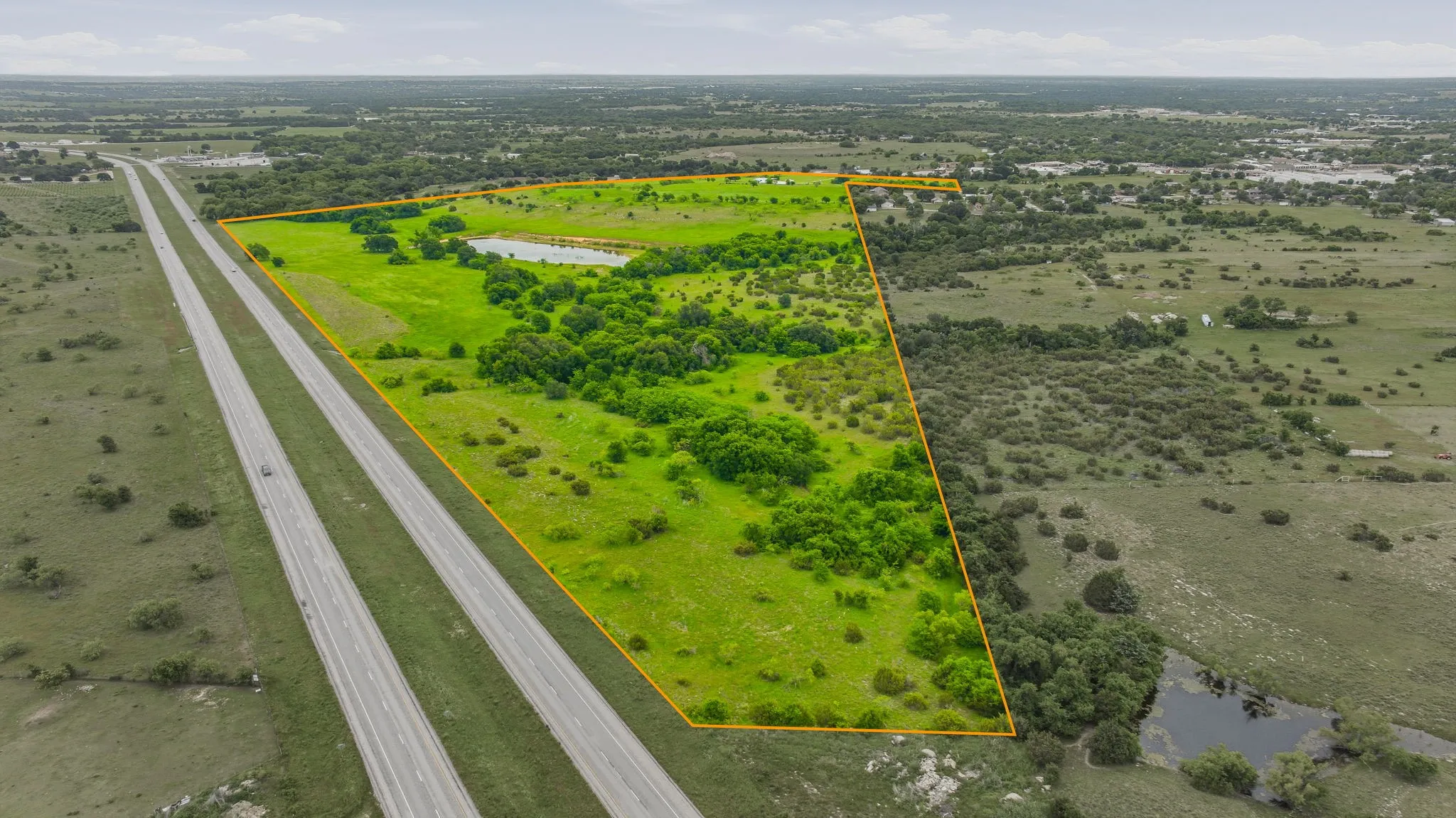 Expansive green landscape with a defined perimeter, featuring a pond, mature trees, and direct frontage on a multi-lane highway