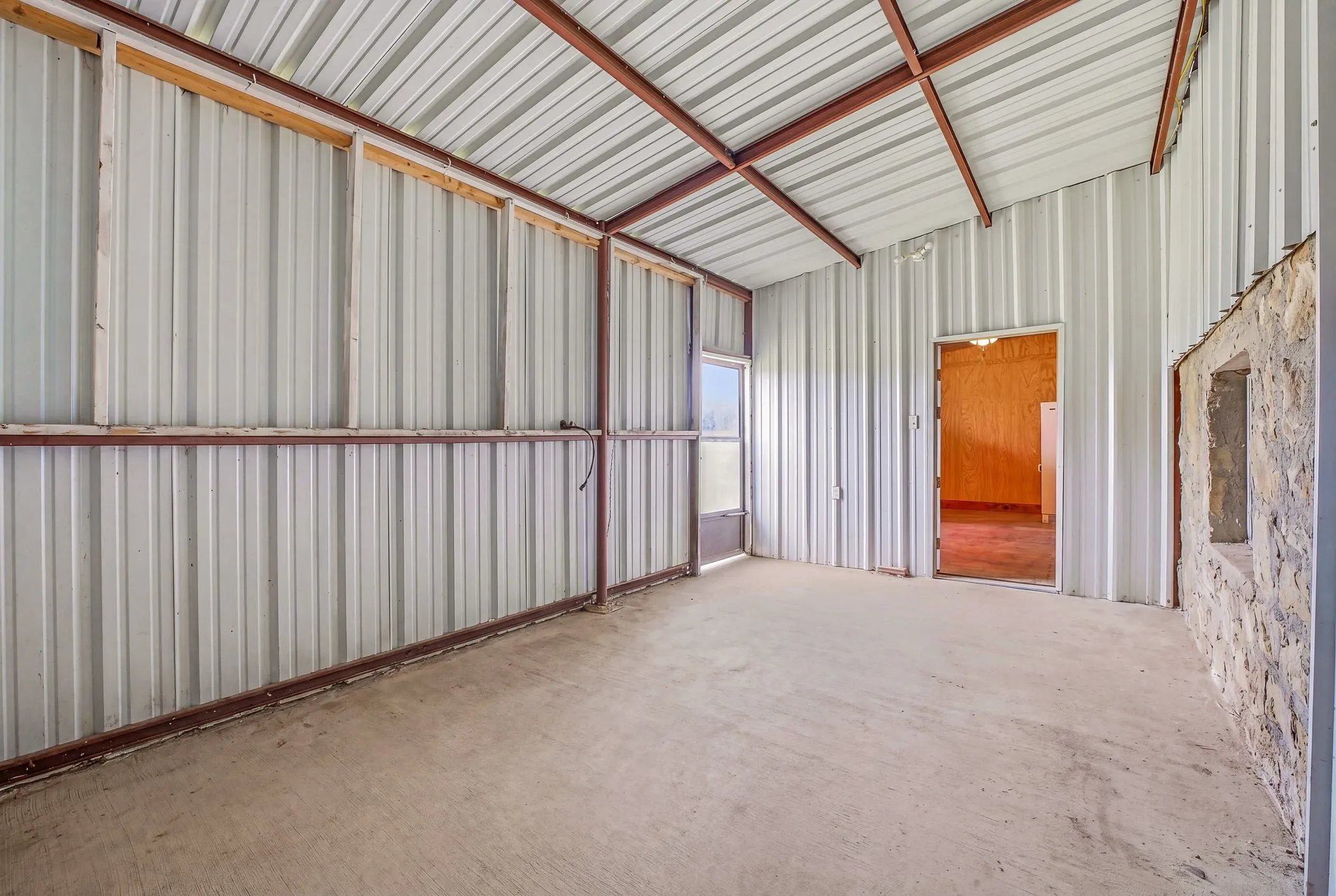 Covered patio featuring a concrete floor, corrugated metal walls, and a pitched roof with exposed metal beams