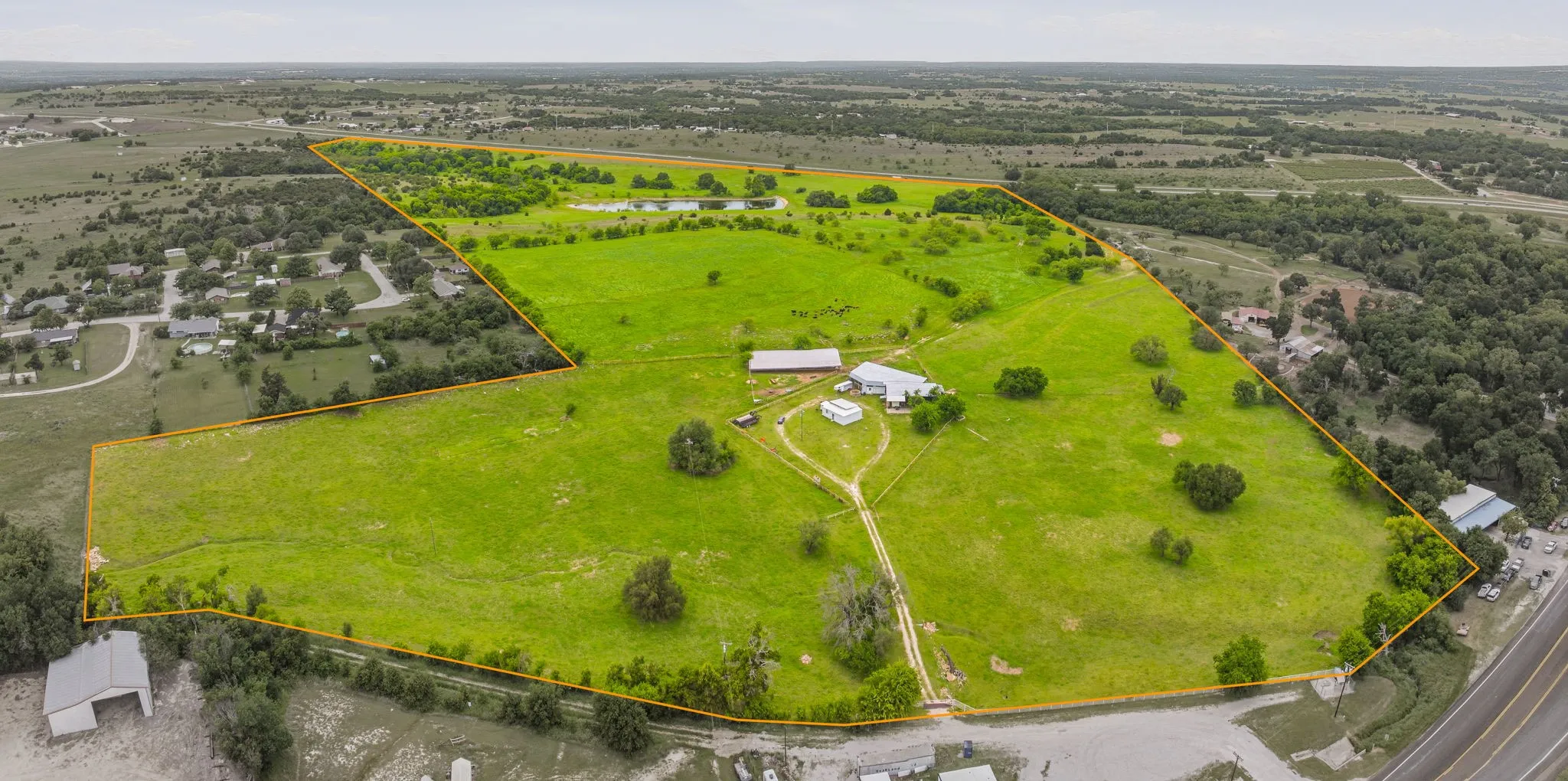 Expansive green acreage featuring a large residential structure, outbuildings, and a pond