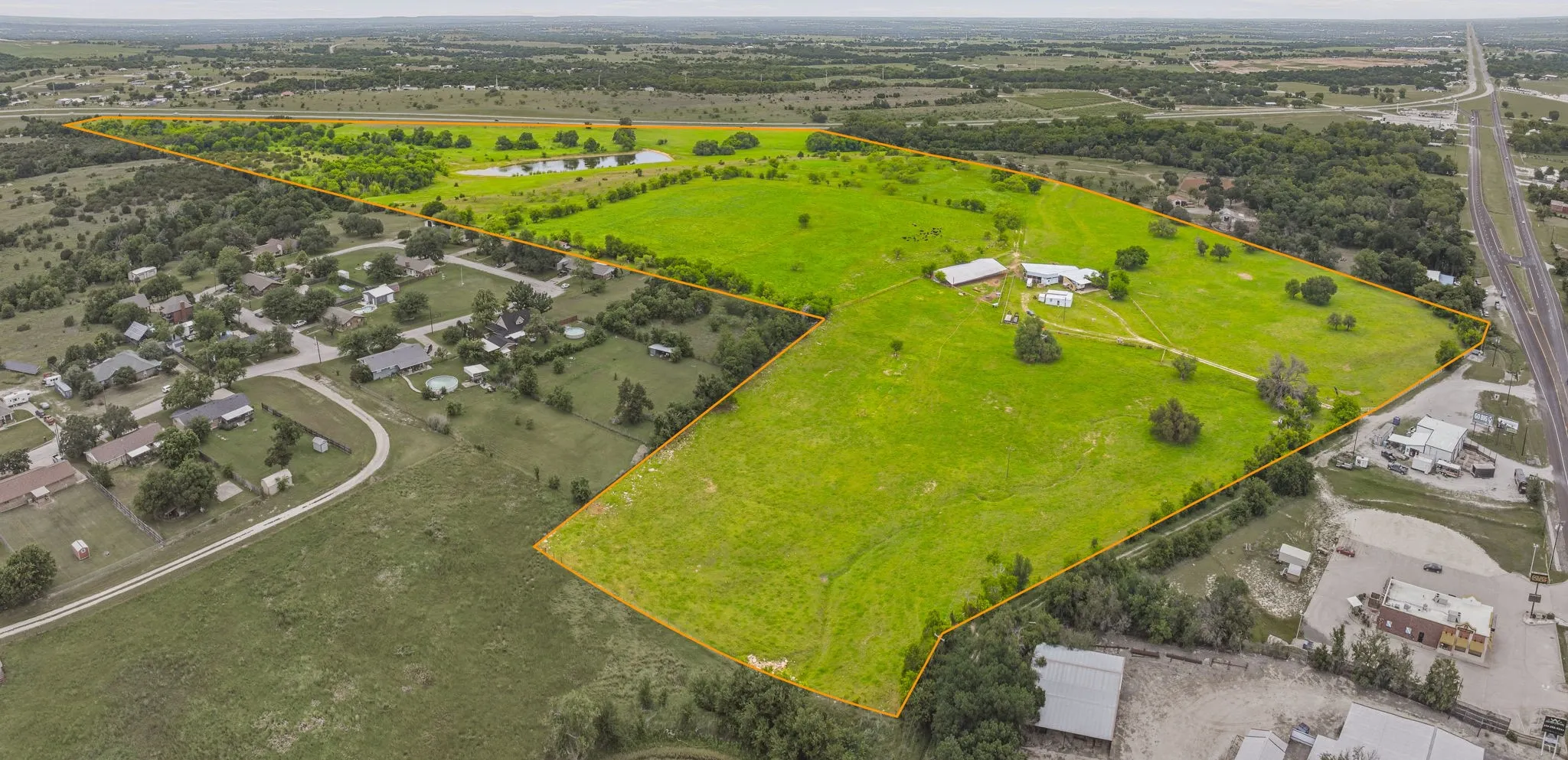 Expansive rural property featuring multiple cleared pasture areas, scattered mature trees, and a pond
