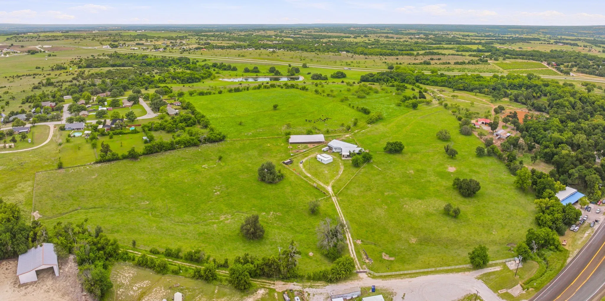 Expansive acreage featuring multiple structures, verdant fields, a primary residence with an attached garage, a barn, and a winding driveway