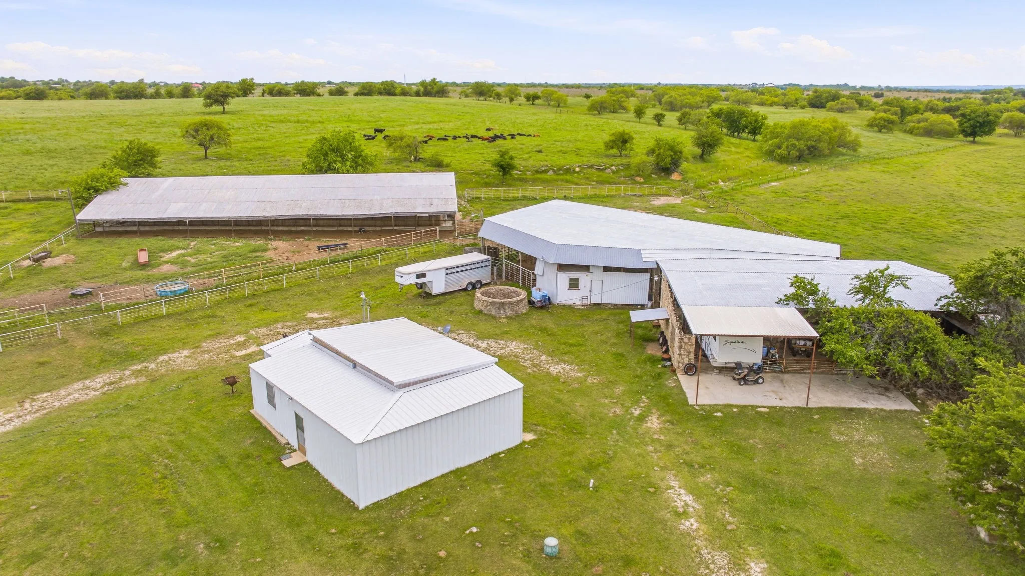 Expansive property featuring multiple metal-roofed structures, including a long agricultural building, a large primary structure with a covered patio, and a separate metal building