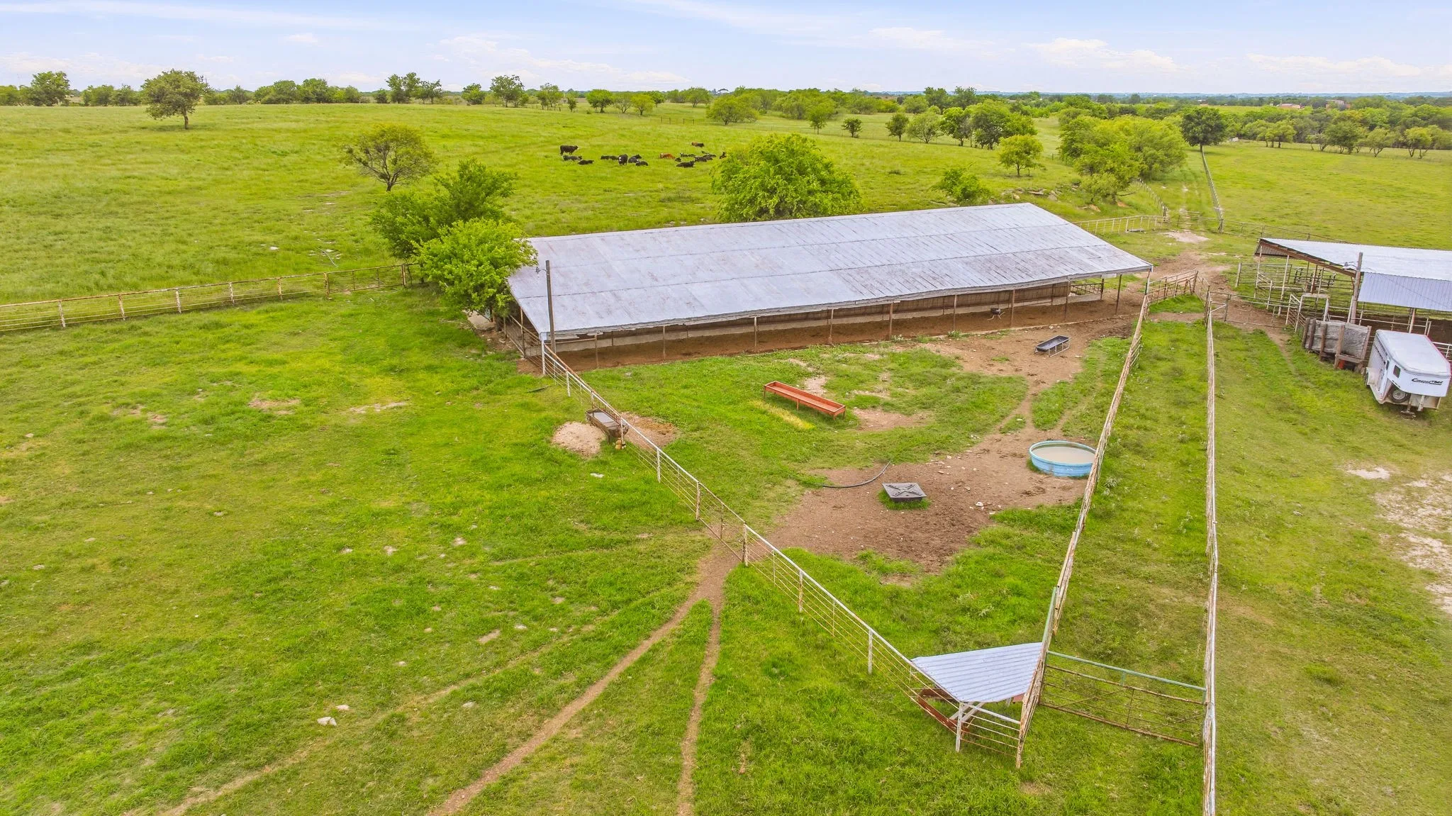 Expansive agricultural property featuring a long, open-sided barn with a corrugated metal roof