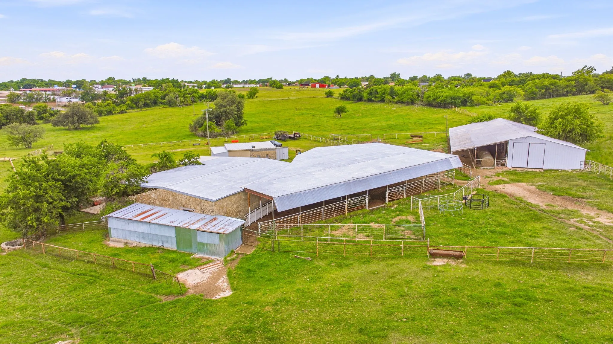 Expansive property featuring multiple structures, including a large white barn with a gambrel roof and a long, open-sided shed with a metal roof