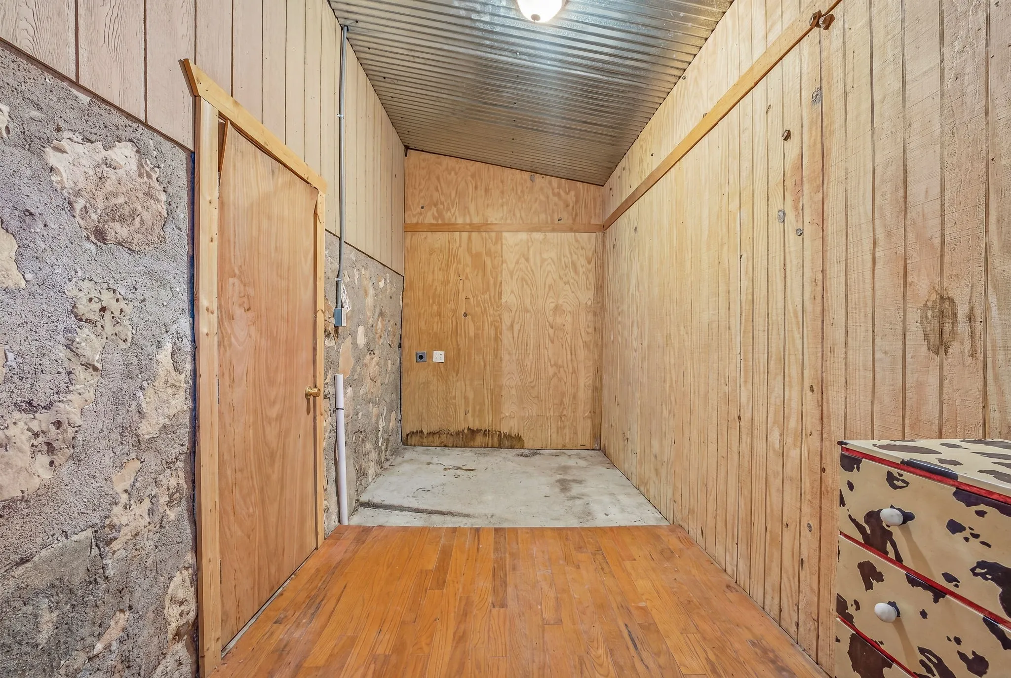 Wood-finish flooring leading to a concrete-floor area with a stone-finish wall and natural wood paneling