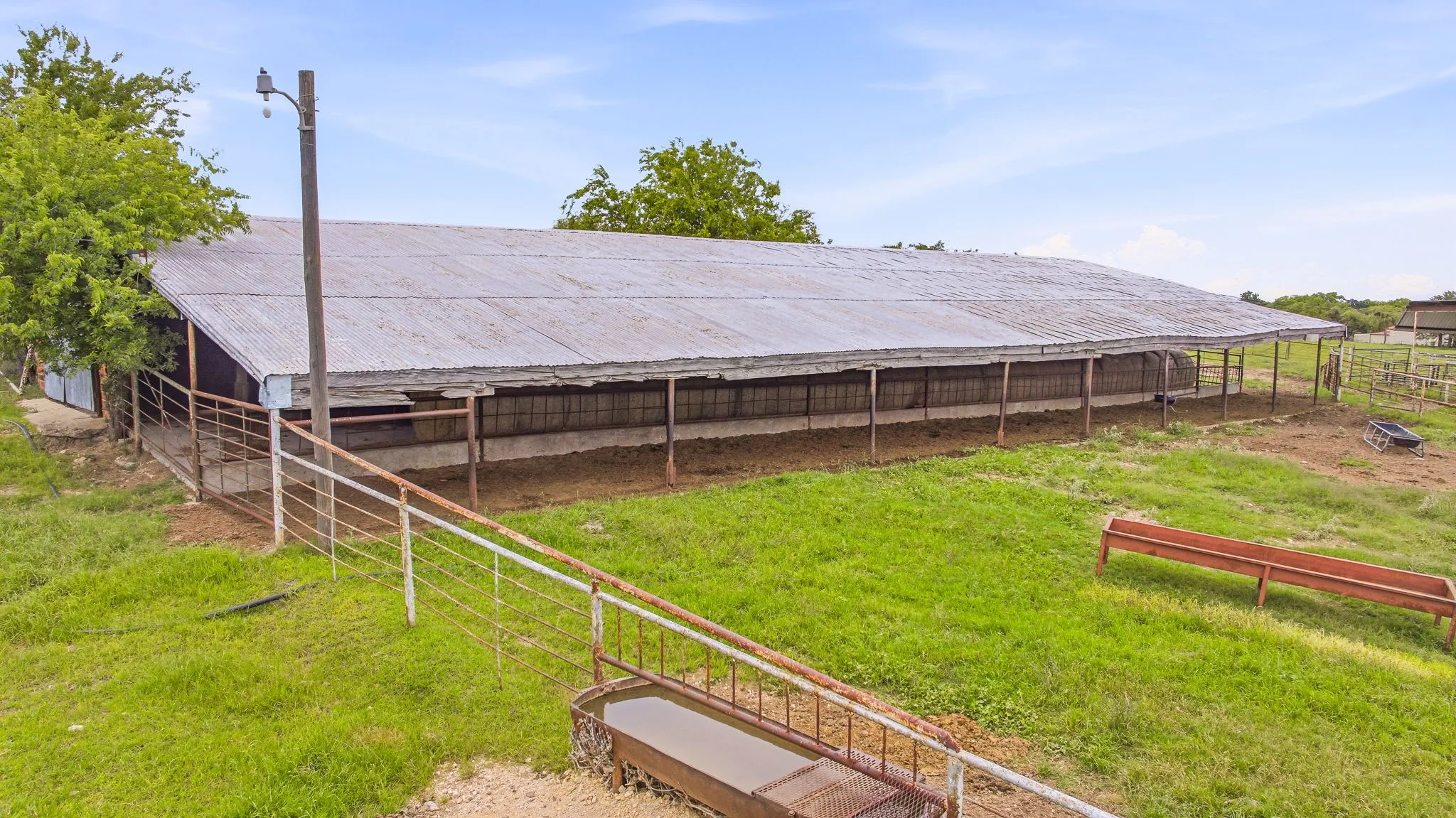 Expansive agricultural building featuring a corrugated metal roof, open-air structure, and surrounding fenced areas