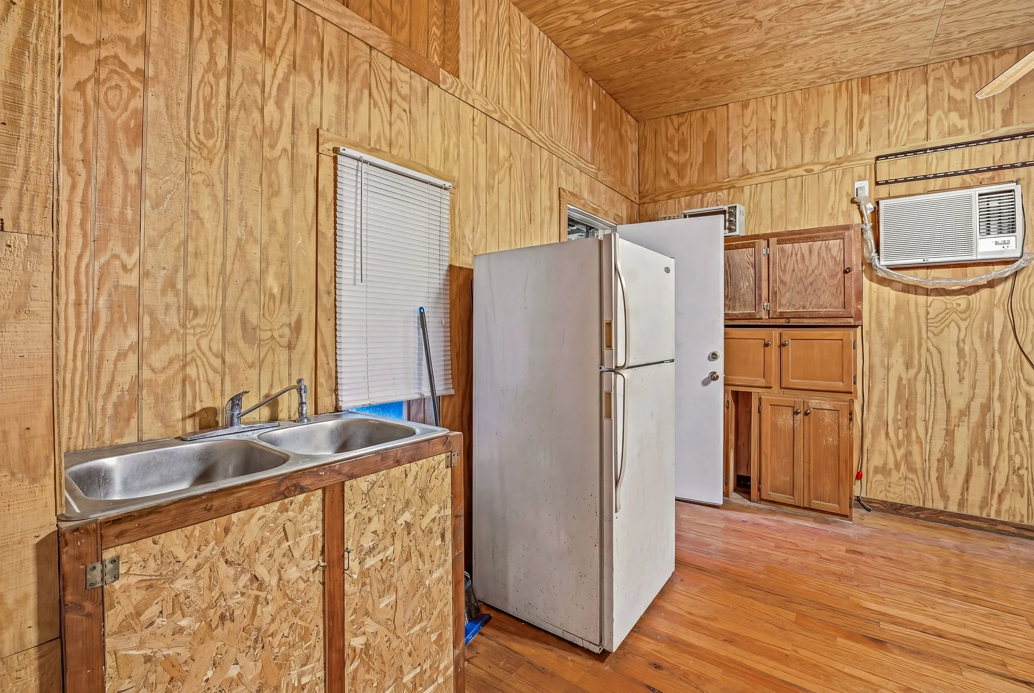 Kitchen area featuring wood-finish flooring, wood panel walls and ceiling, a built-in double stainless steel sink, and wood cabinetry