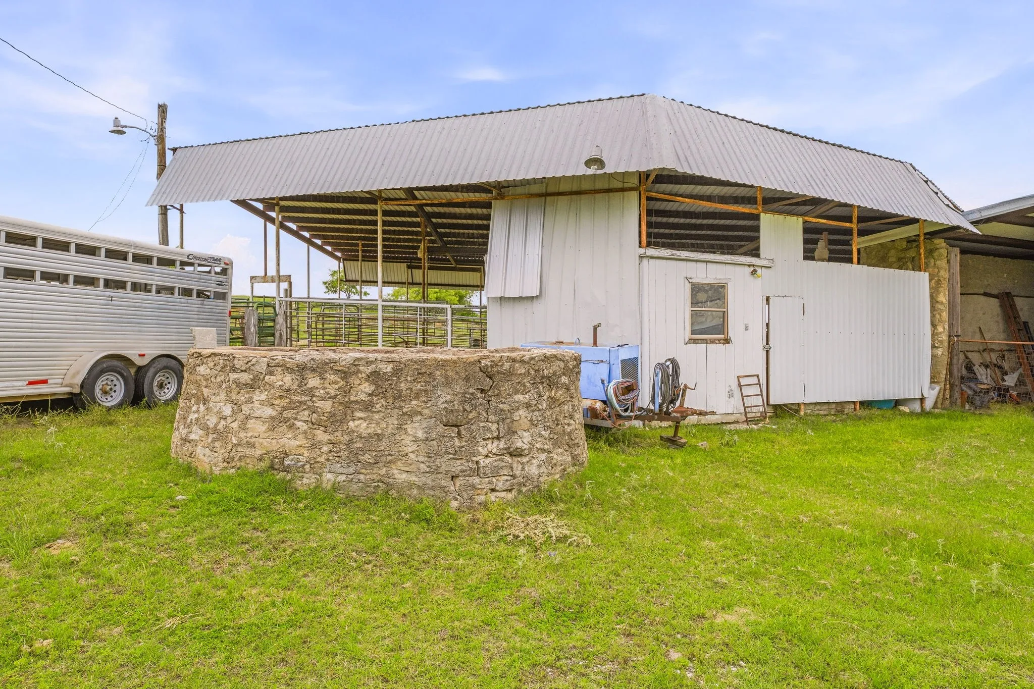 Stone-built structure in a grassy area, featuring a metal-roofed barn with white siding and open-air sections