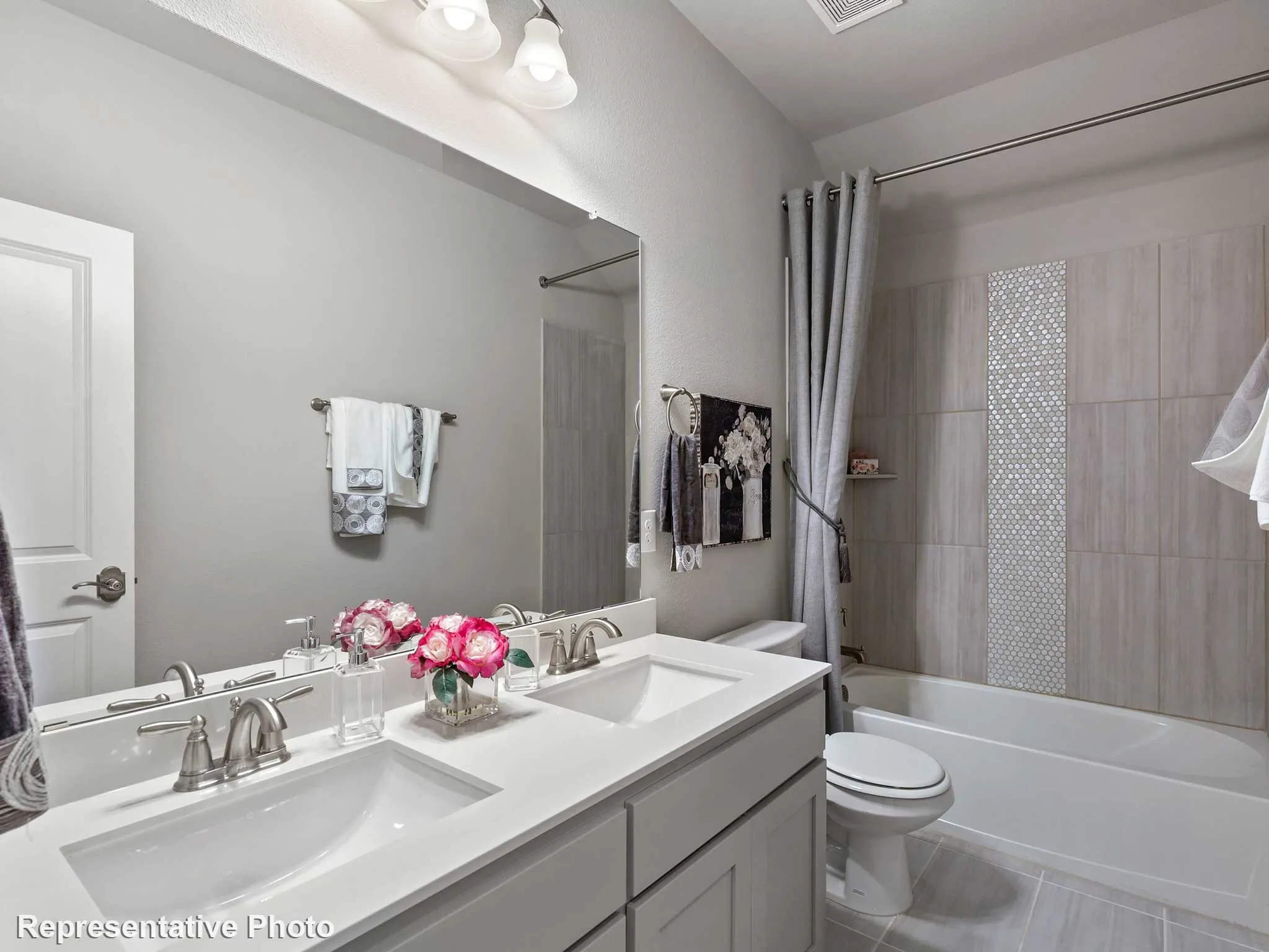 Bathroom featuring a dual vanity with undermount sinks and brushed nickel fixtures, a tub/shower combination with subway tile surround, a decorative mosaic tile accent, and light gray tile flooring