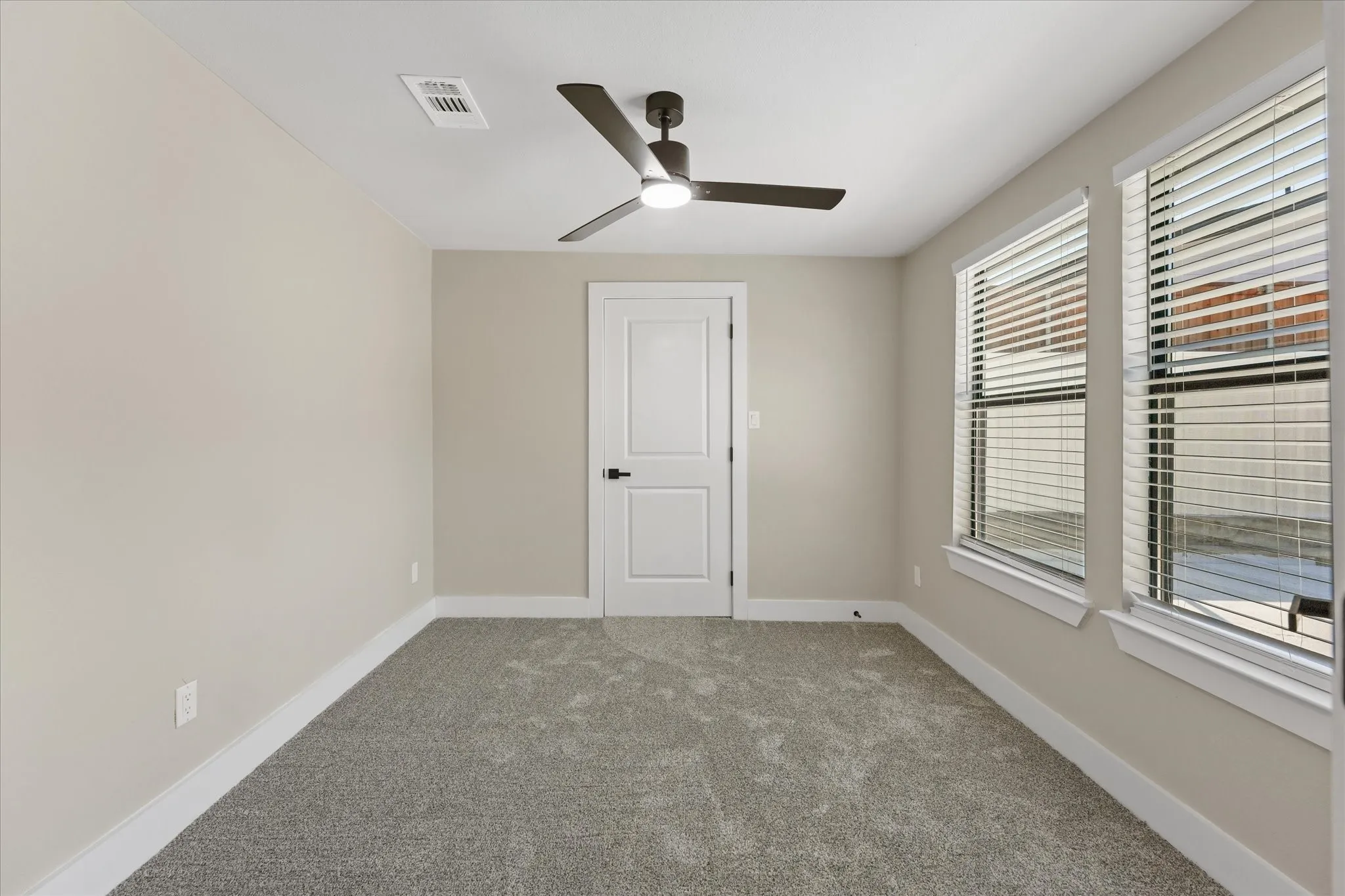 Room #3, Neutral-toned room featuring a ceiling fan with integrated lighting, two windows with blinds, a white paneled door, and gray carpet flooring