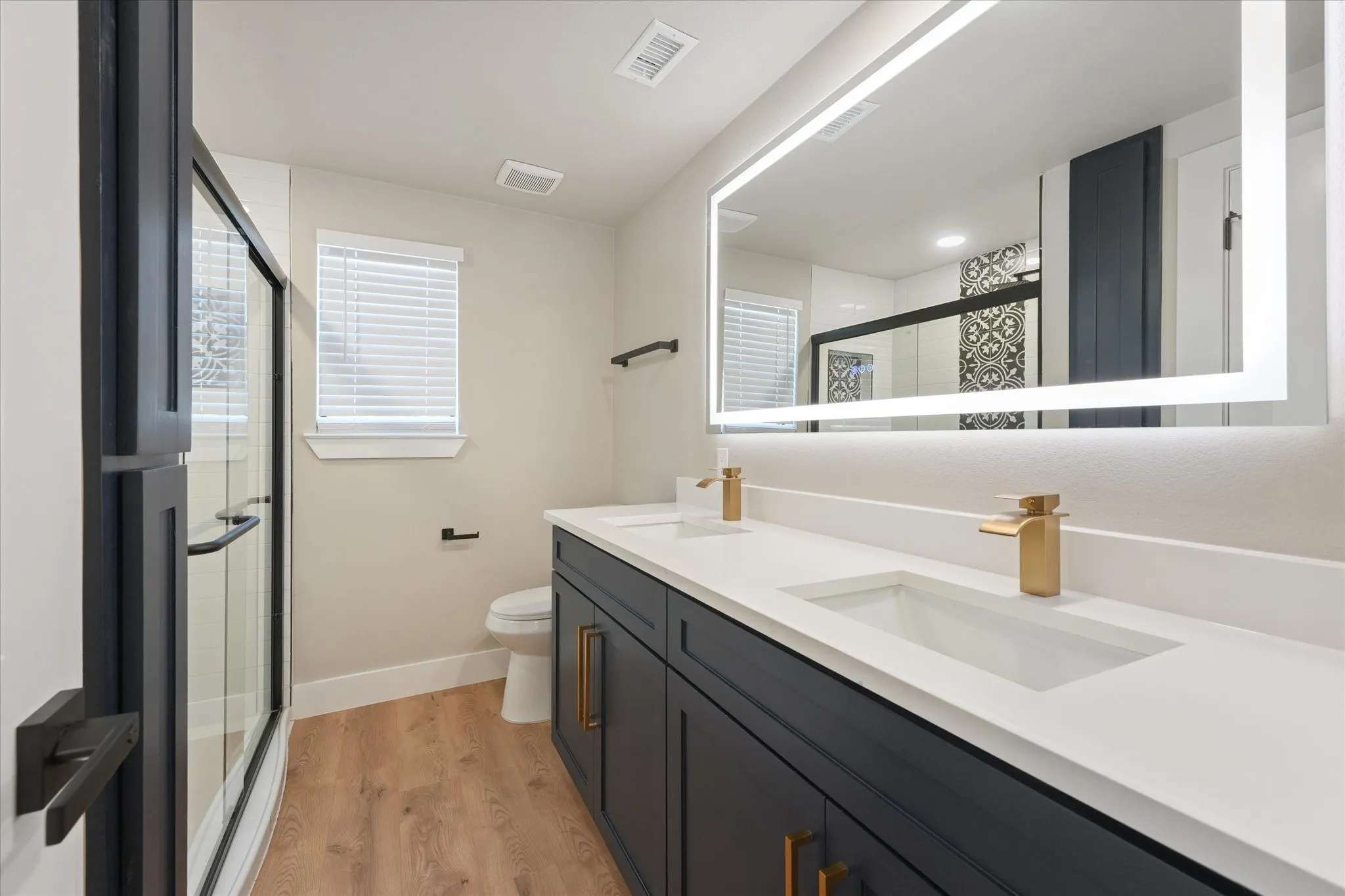 Dual sink vanity with white countertop, brass fixtures, and dark cabinetry