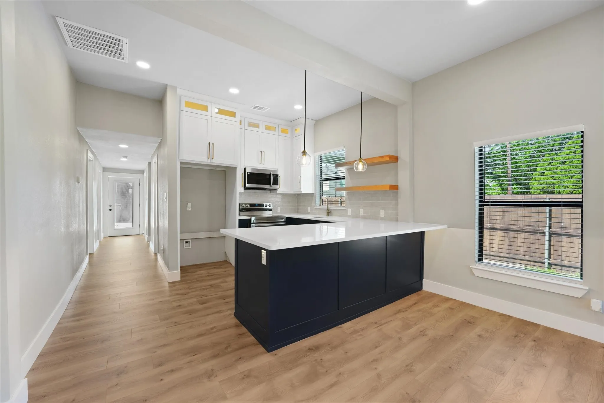 Open-concept kitchen featuring a dark blue island with a white countertop, white upper cabinetry with gold-toned accents, stainless steel appliances.