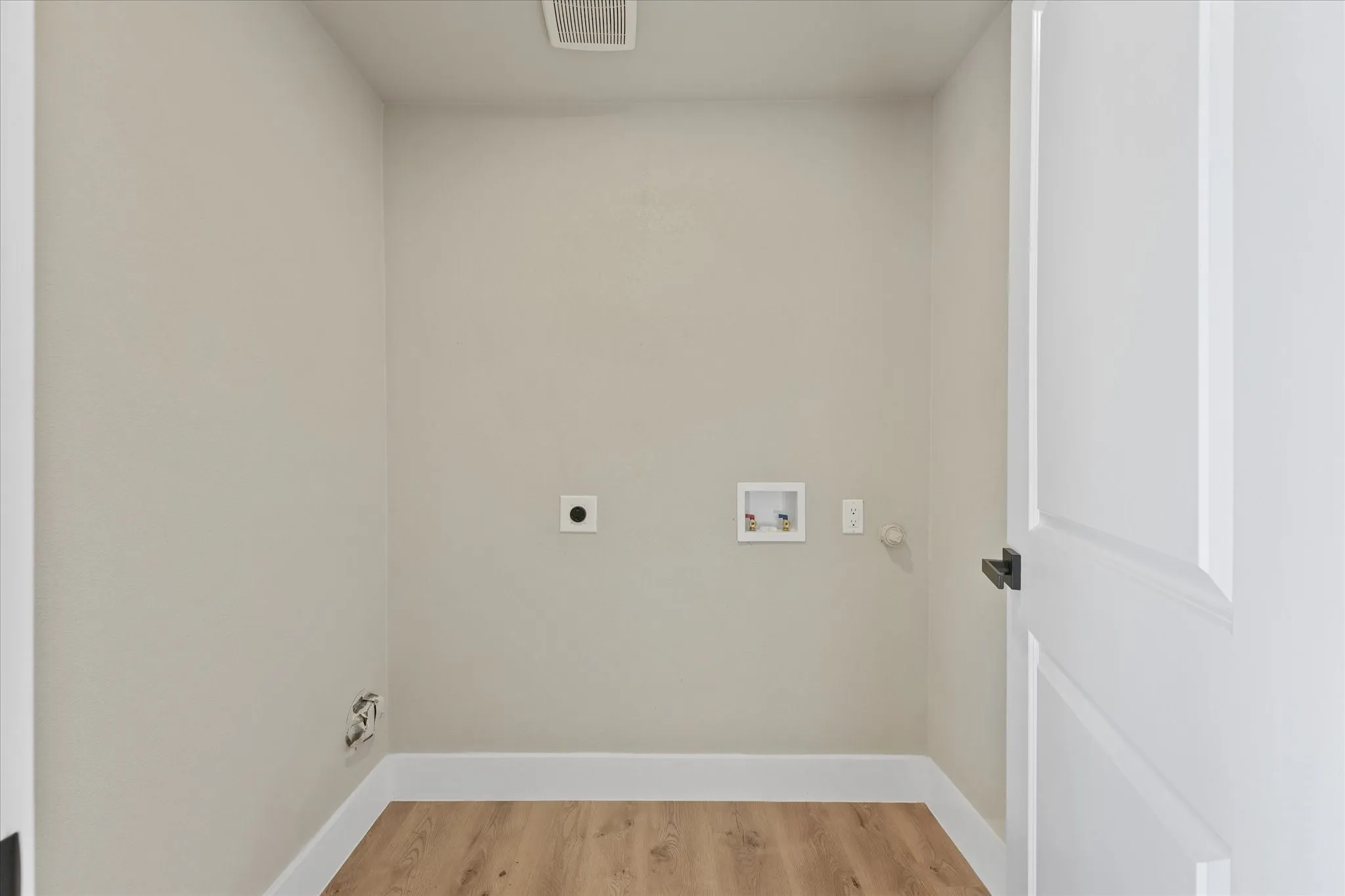 Dedicated laundry area featuring light-toned walls, white baseboards, and a white paneled door with a black handle