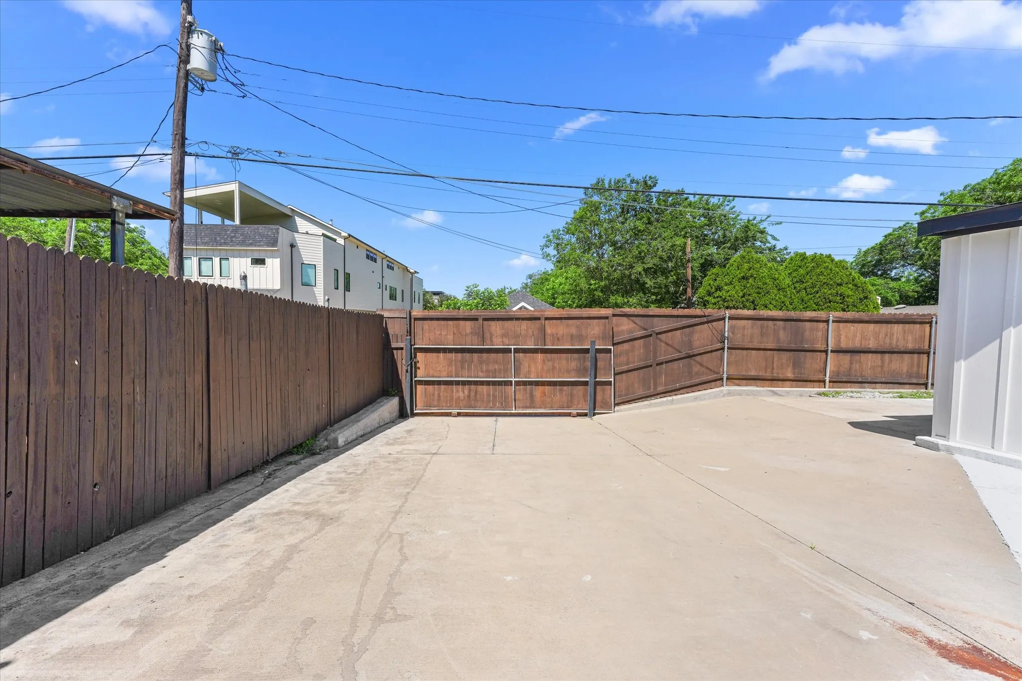 Paved outdoor area featuring a stained wood privacy fence and a white vertical siding structure