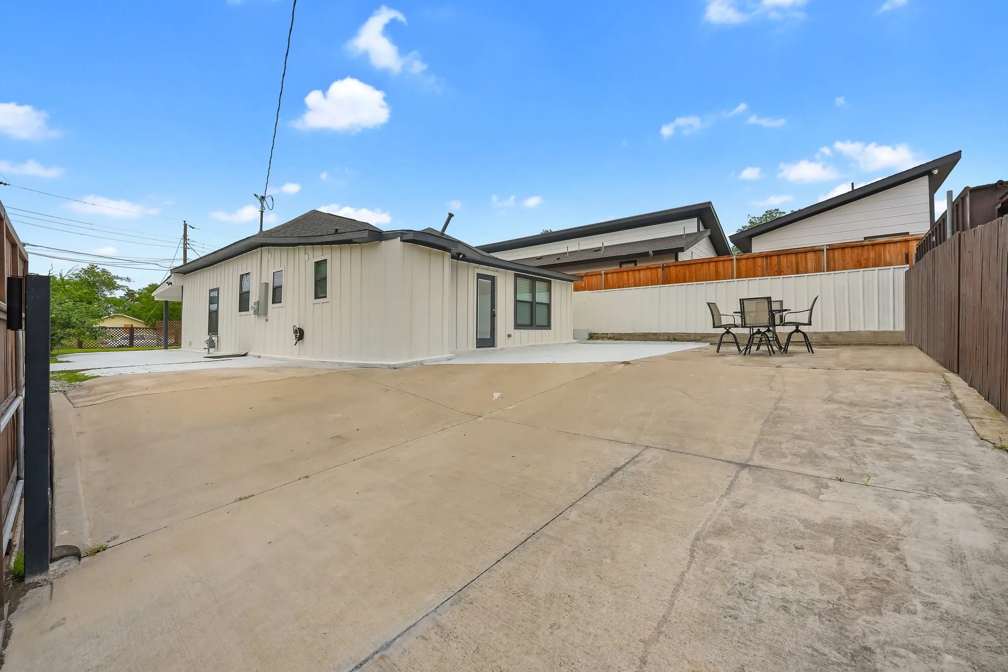 Expansive concrete patio area with a white vertical panel exterior and a dark roofline. Ample parking spaces.