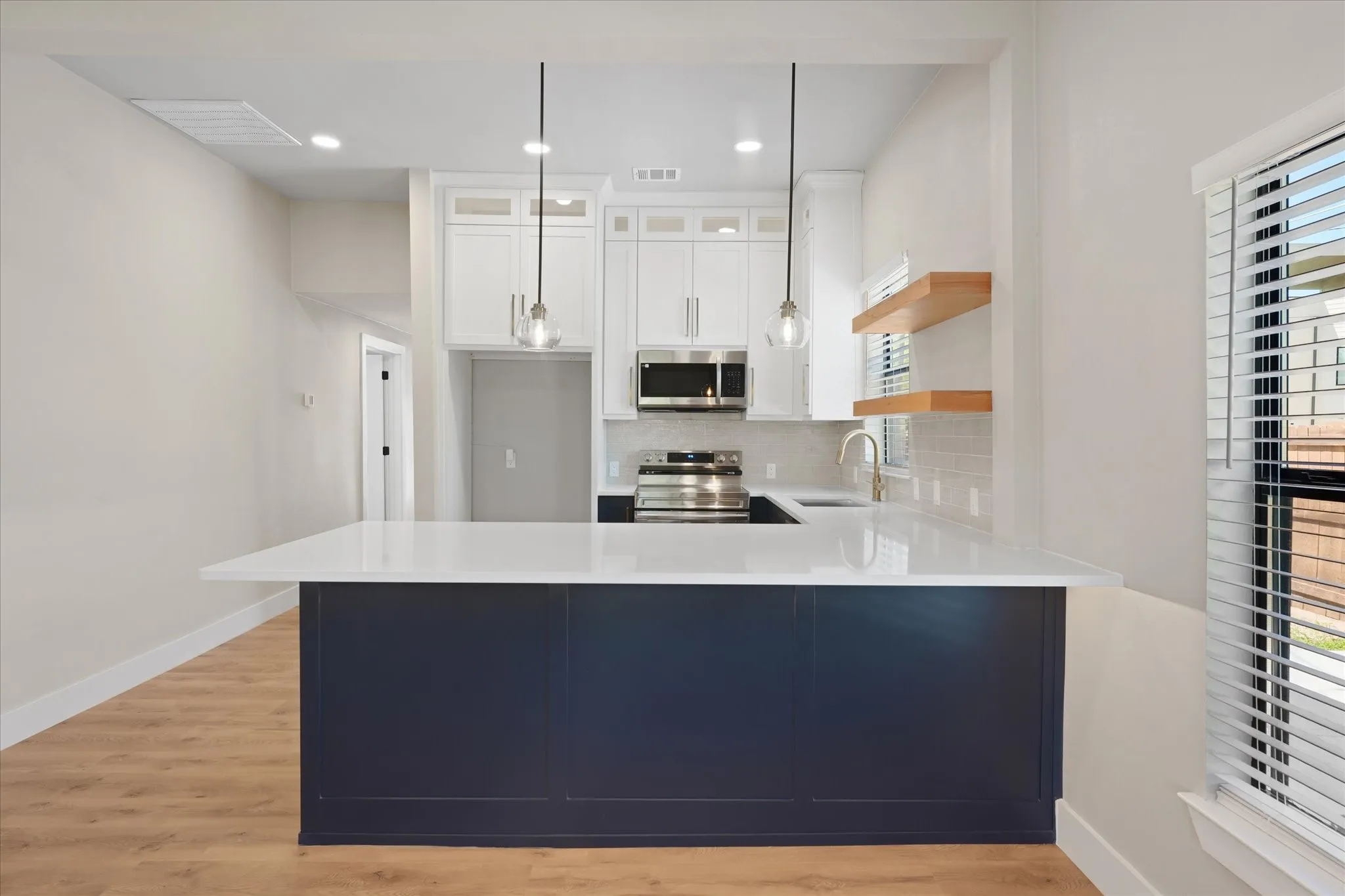 Kitchen featuring a large island with a dark blue base, white countertop, and two pendant lights