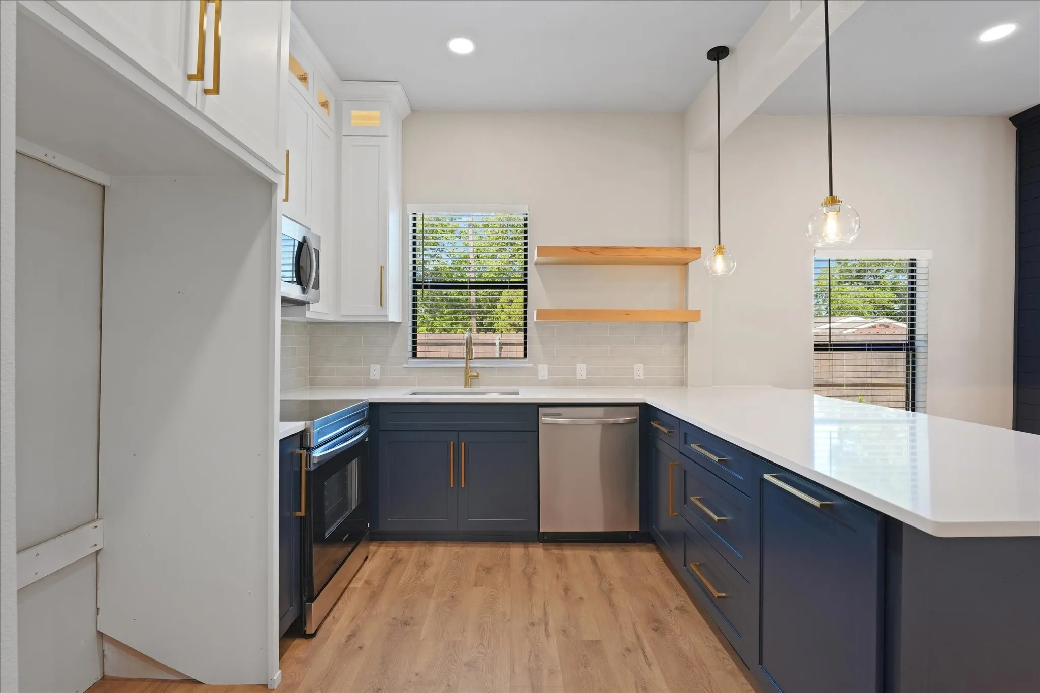 Contemporary kitchen featuring white shaker upper cabinetry and dark blue lower cabinetry, white countertops, stainless steel appliances, and wood-finish flooring