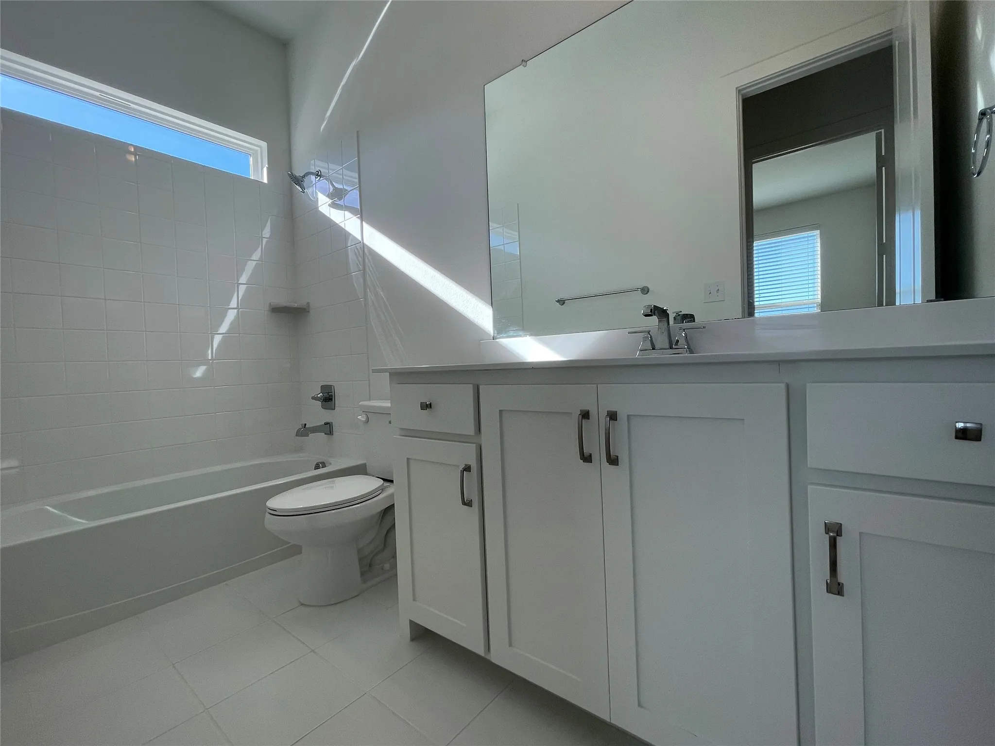 Modern bathroom featuring a white vanity with shaker-style cabinetry, a vanity mirror, a bathtub with a shower, and a high window