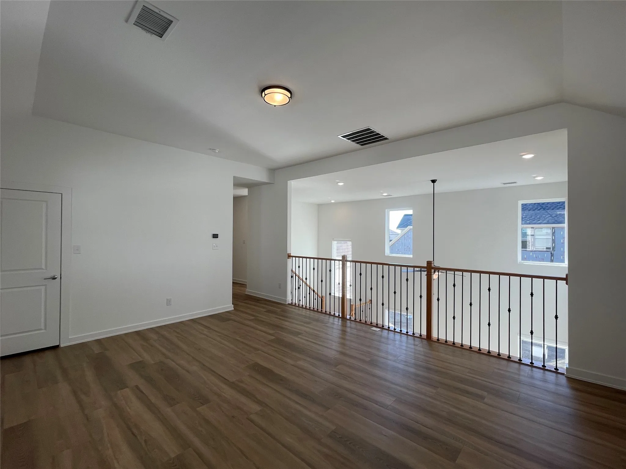 Spacious loft area featuring wood-finish flooring, white walls, and a contemporary ceiling light fixture