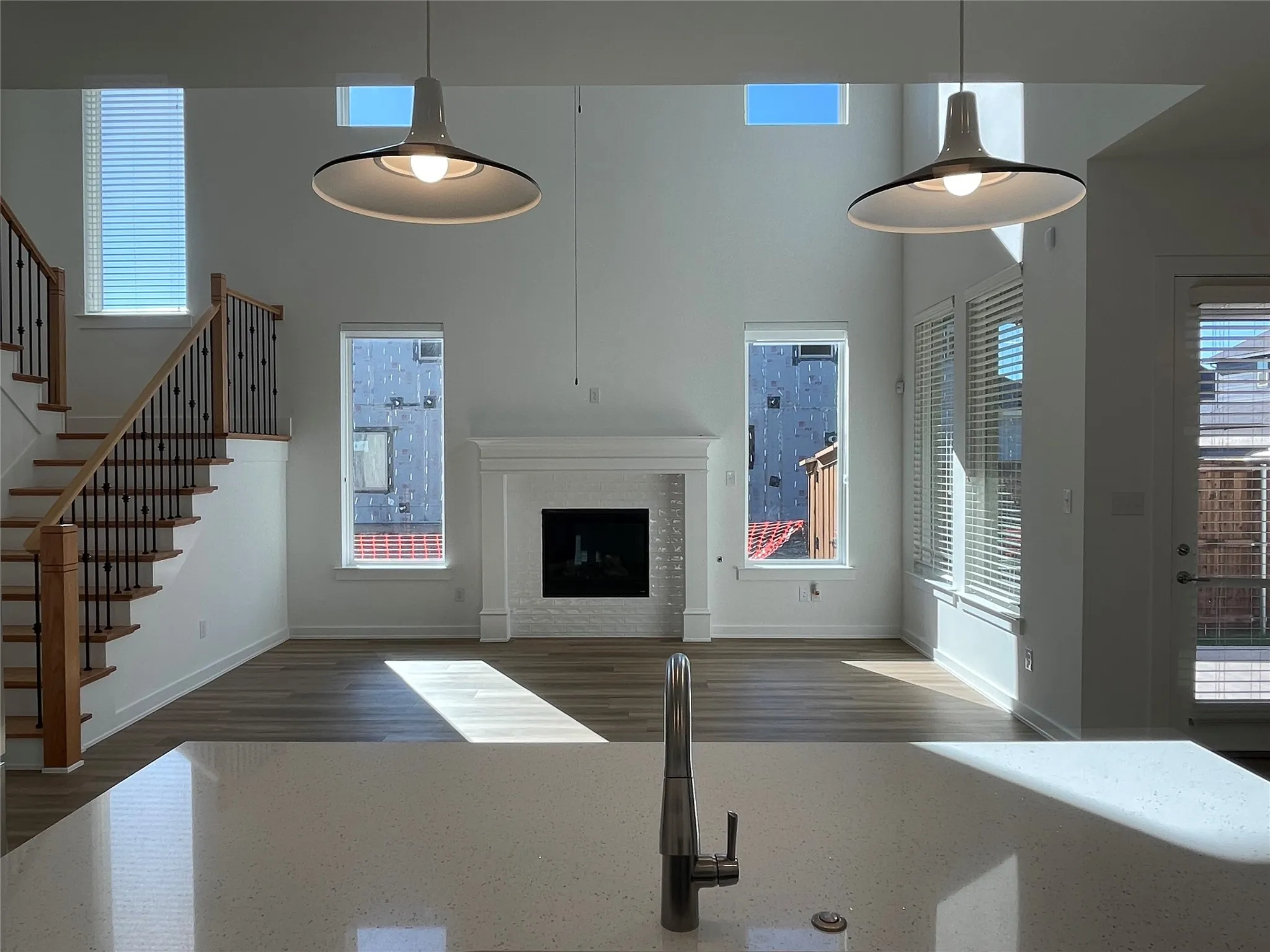 Open-concept living area featuring a fireplace with a white mantel, wood-finish flooring, and a two-story ceiling with pendant lighting