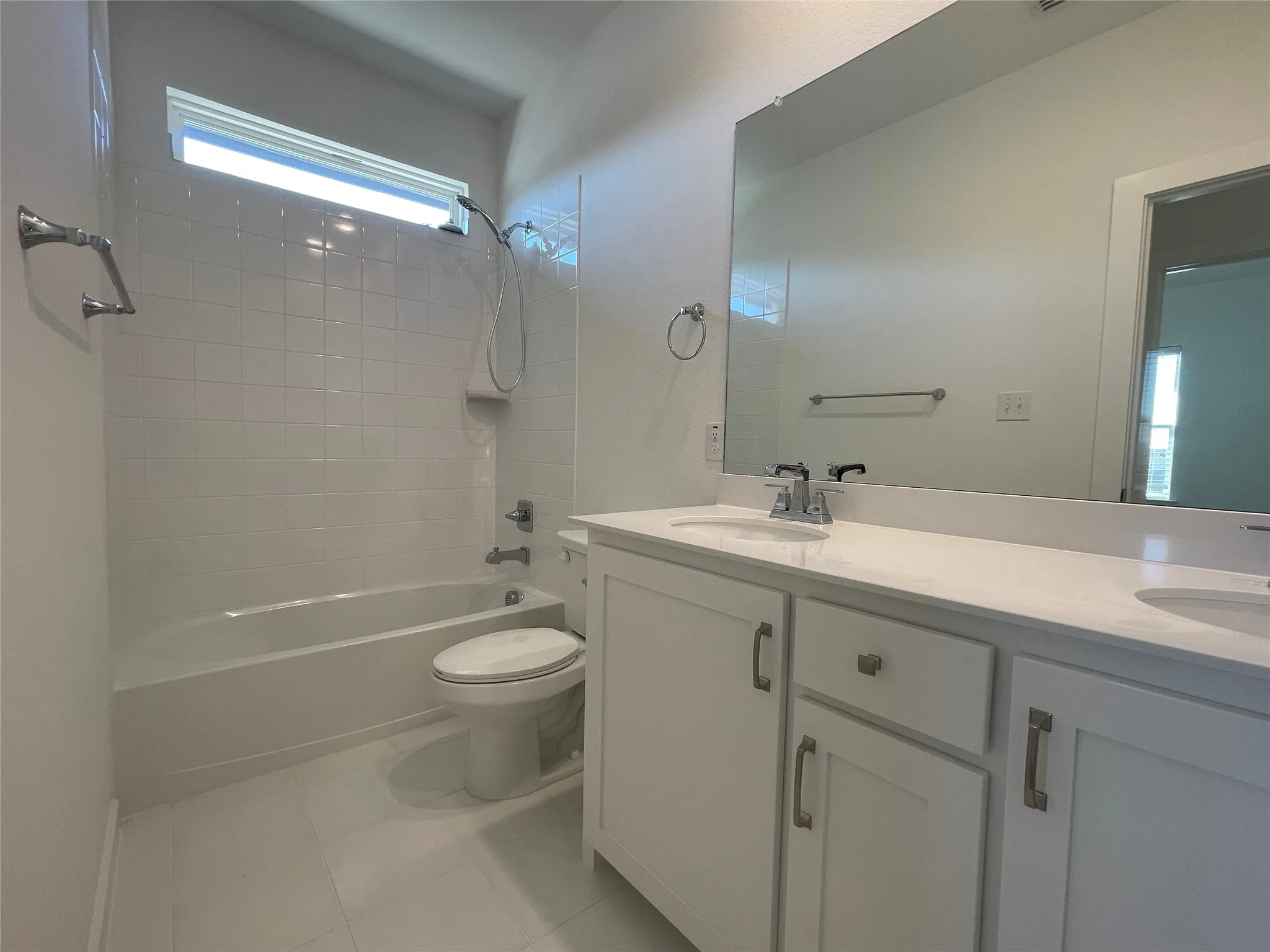Bathroom featuring a double vanity with white cabinetry, a spacious mirror, and a combination tub/shower with white subway tile surround and a transom window