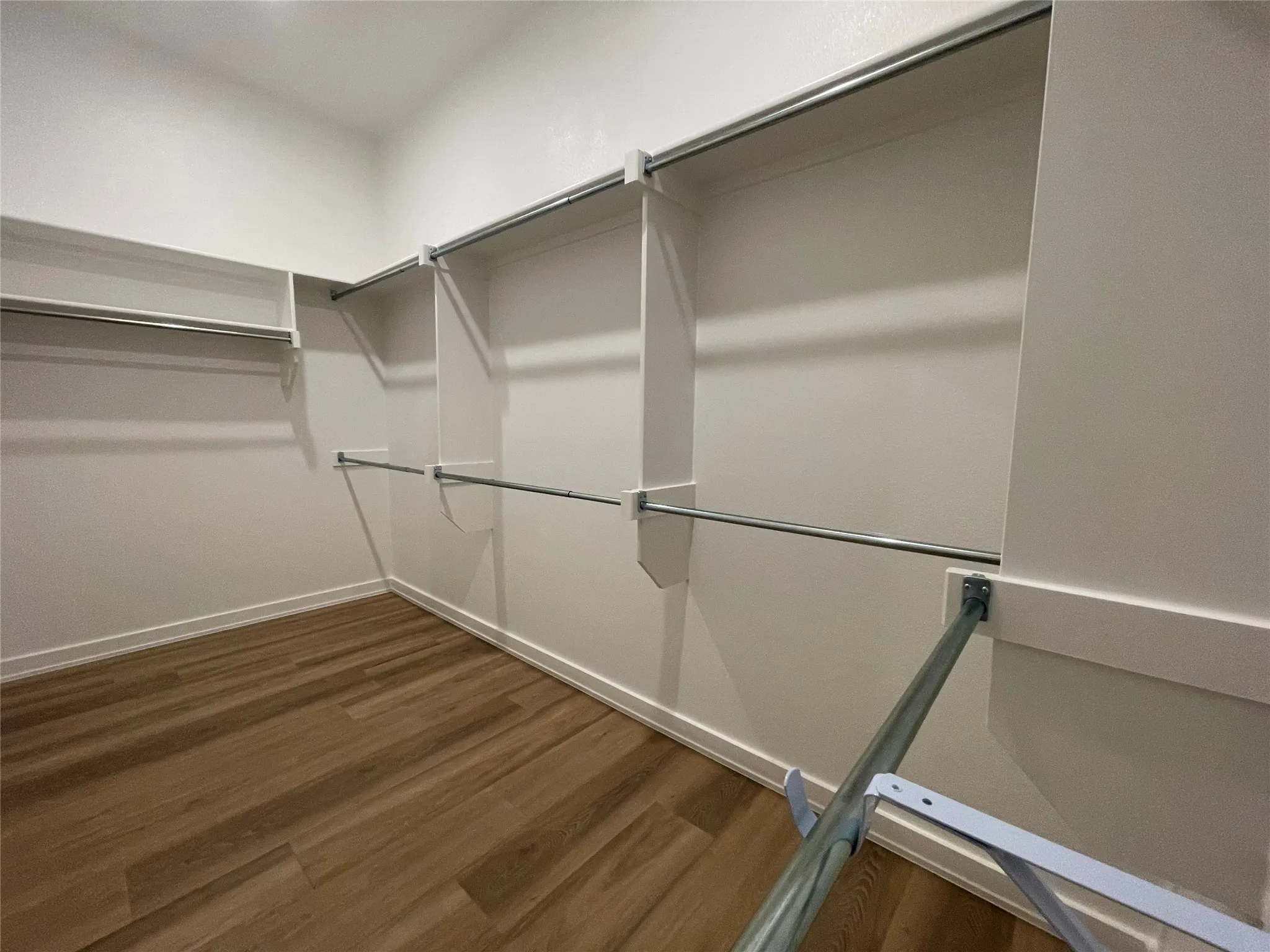 Expansive walk-in closet featuring wood-finish flooring, white walls, built-in shelving, and multiple clothing rods