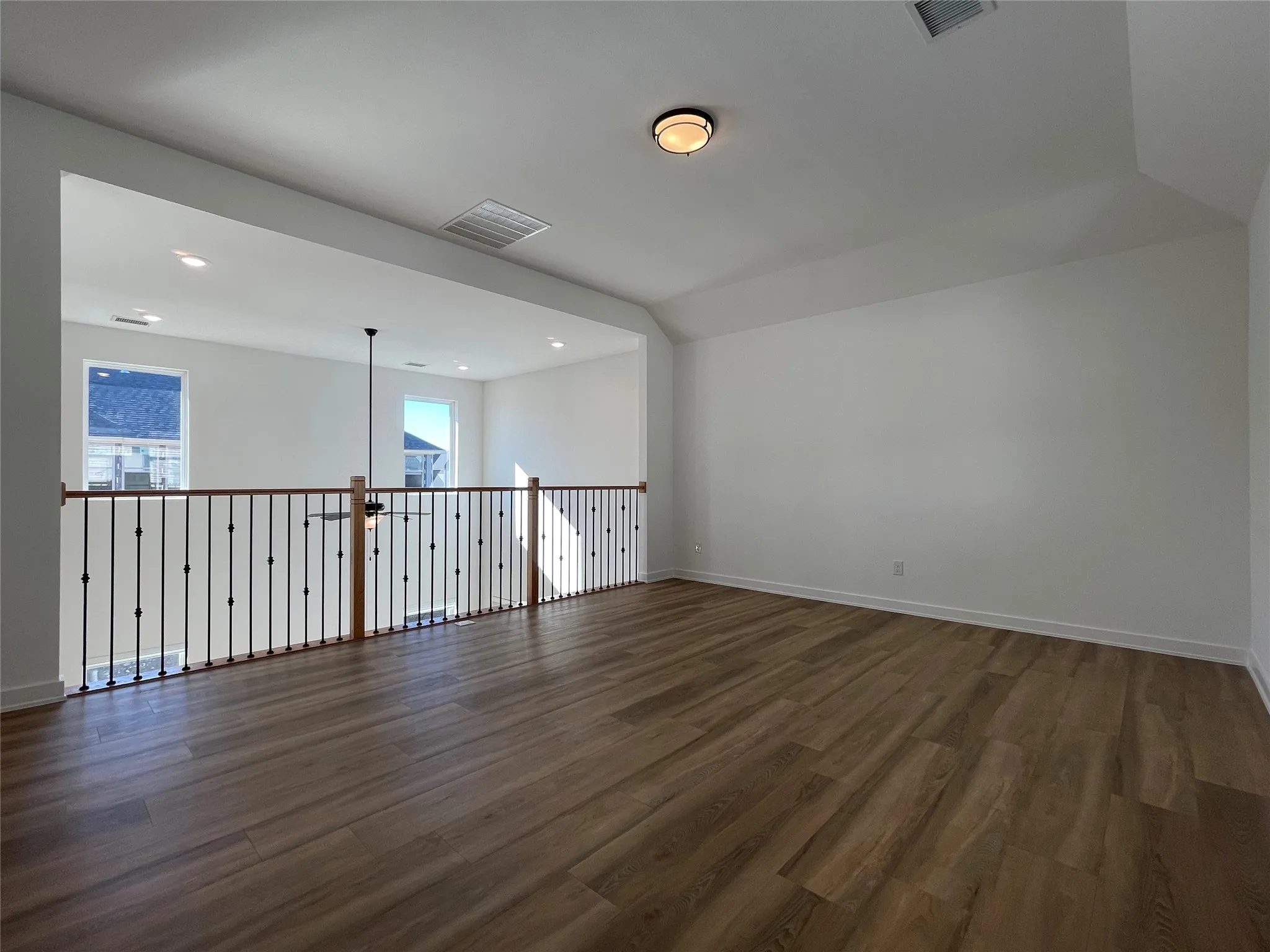 Open loft area with wood-finish flooring, white walls, and a recessed ceiling fan