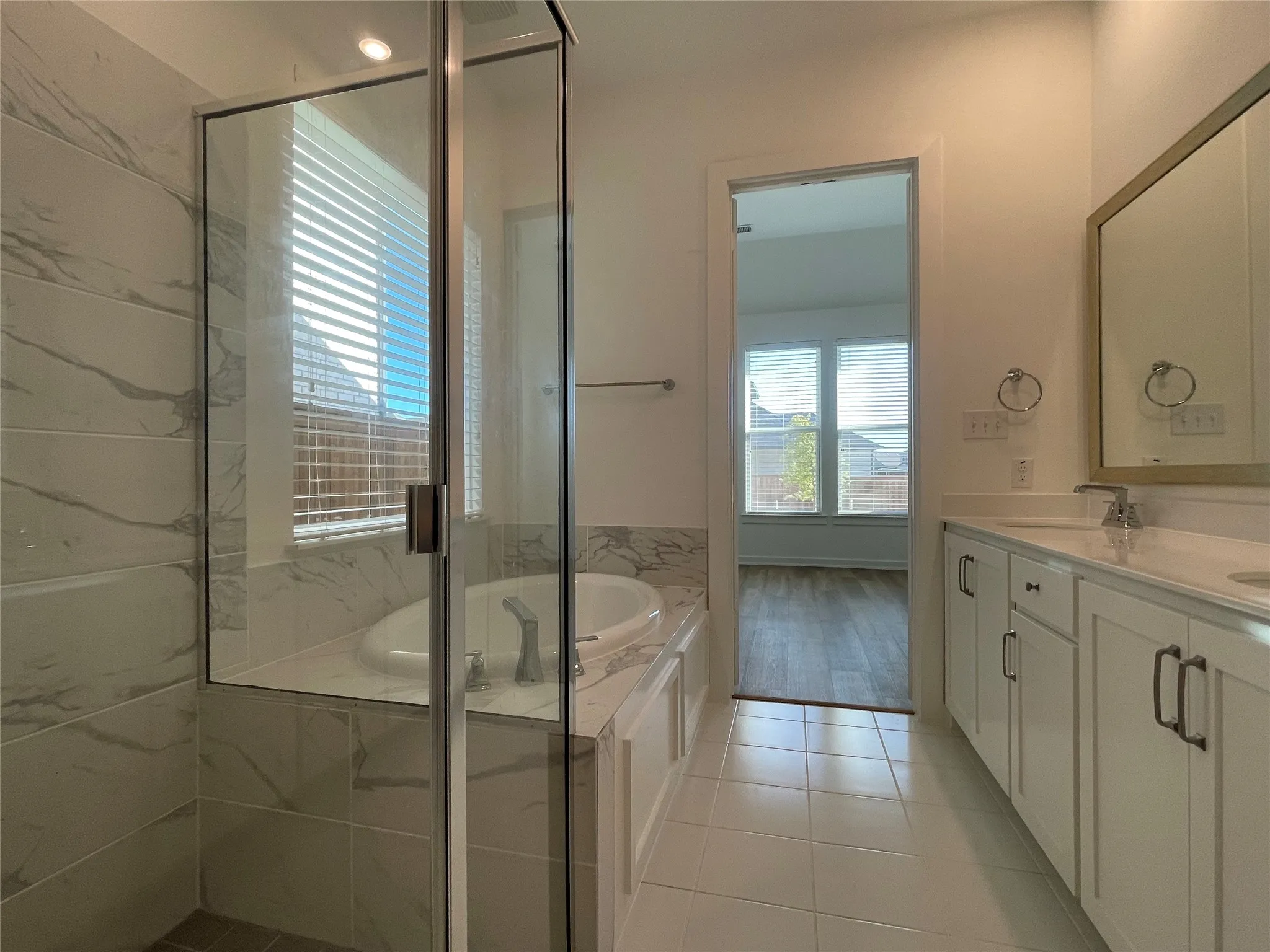 Spacious bathroom featuring a glass-enclosed shower, built-in soaking tub, a double vanity with ample storage, and ceramic tile flooring