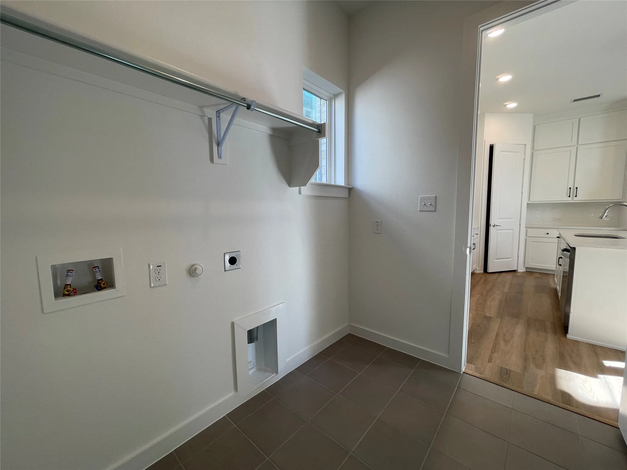 Dedicated laundry area featuring a window, tile flooring, and a chrome hanging rod