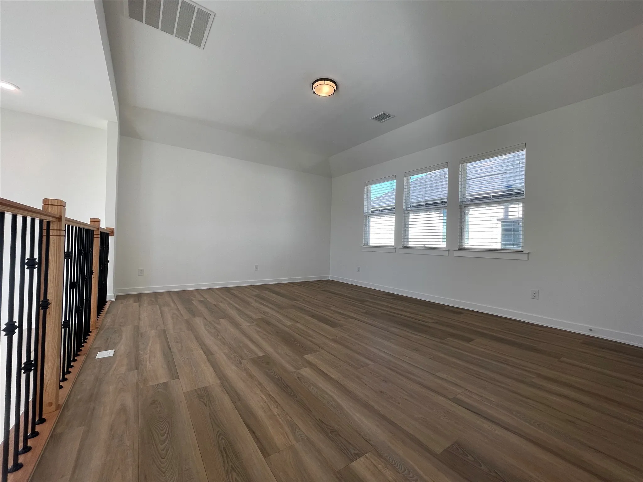 Spacious room featuring wood-finish flooring, white walls, and a recessed ceiling vent