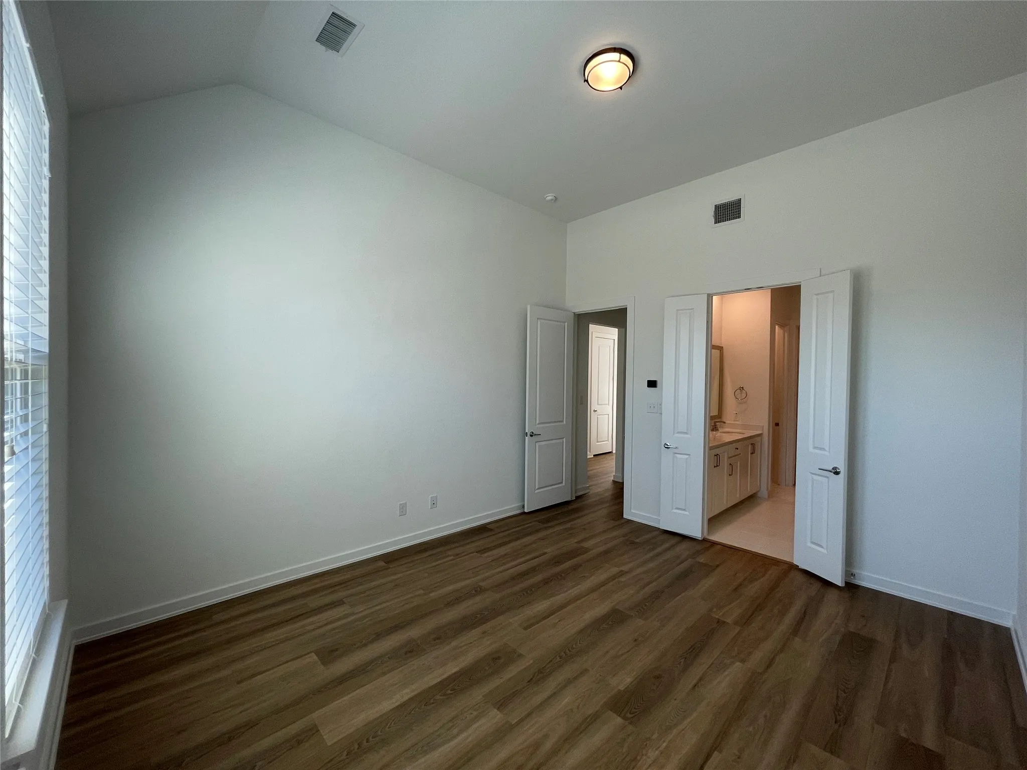 Spacious room featuring vaulted ceilings, wood-finish flooring, and white wall finishes
