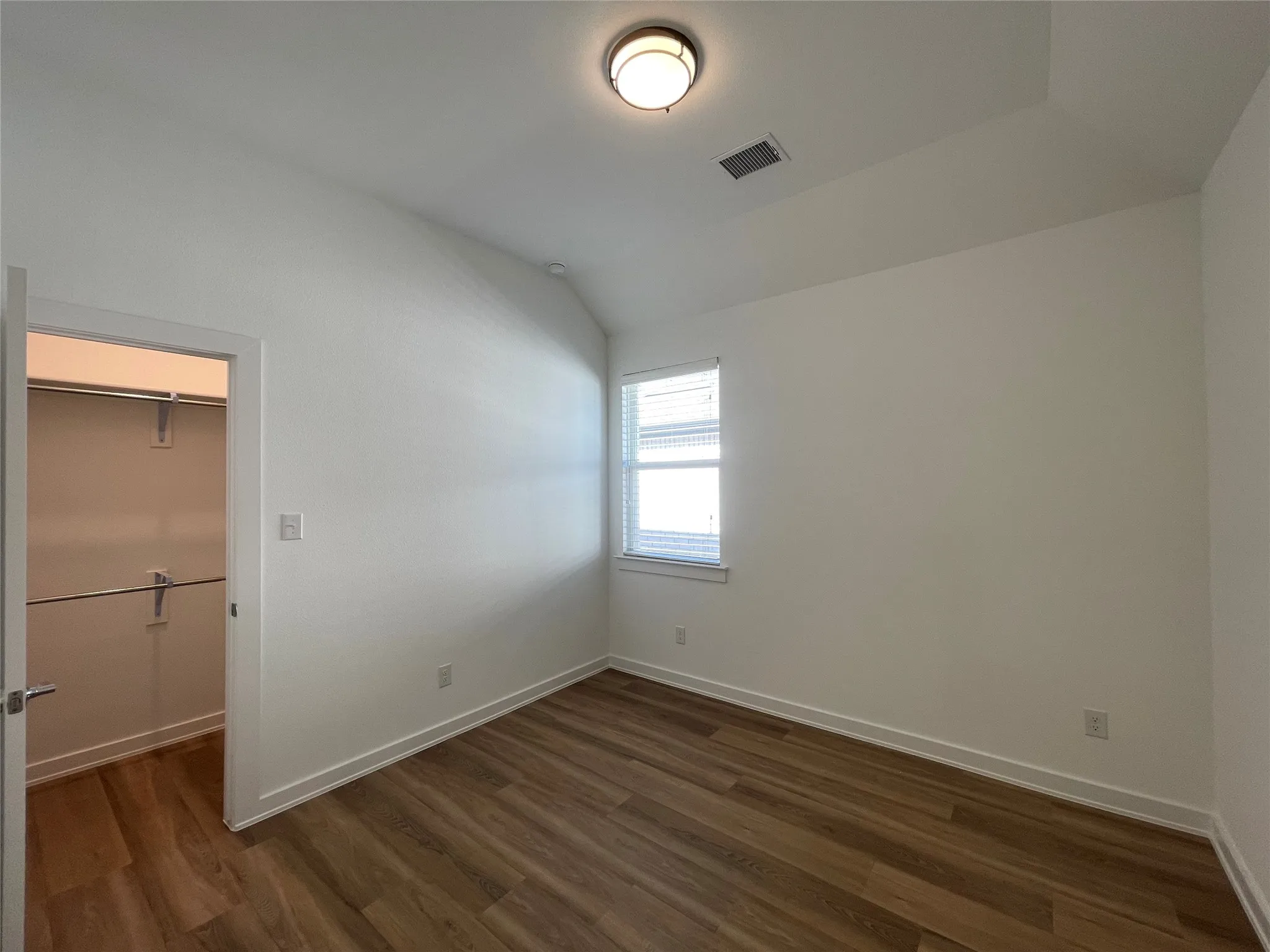 Interior room featuring wood-finish flooring, white walls, and a recessed window with blinds