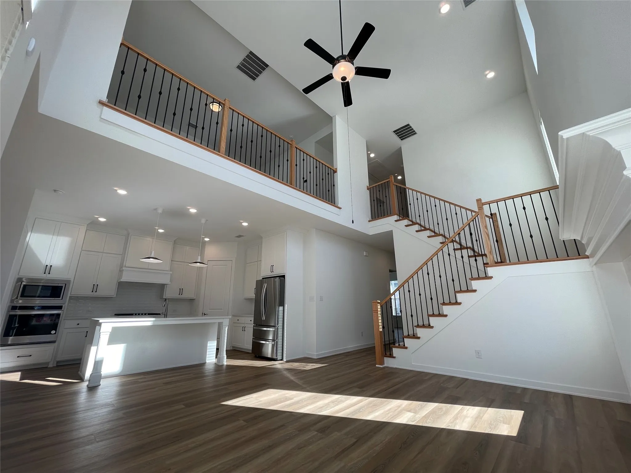 Open-concept living space featuring wood-finish flooring, a two-story ceiling, and a modern kitchen with white cabinetry and stainless steel appliances