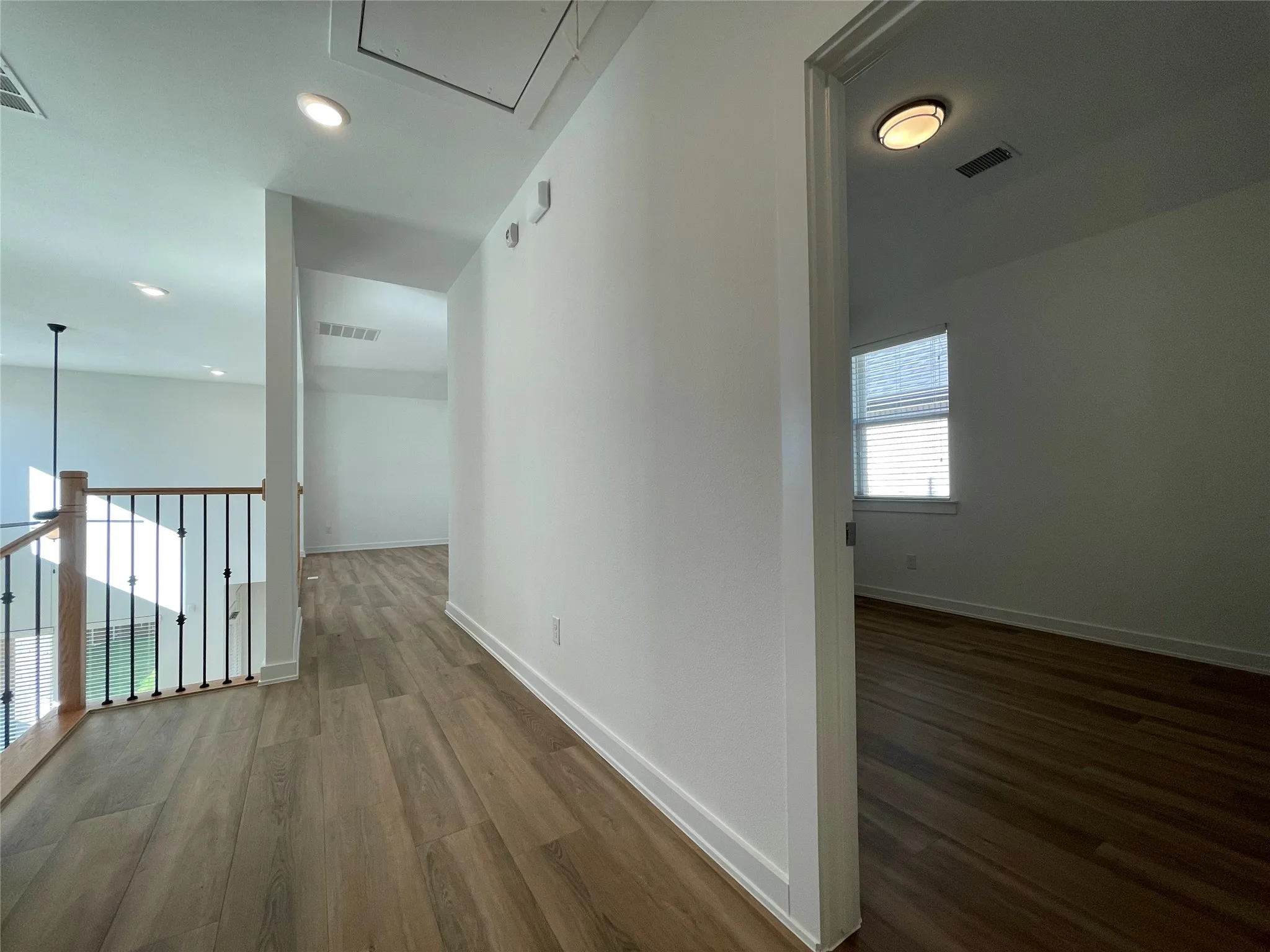 Upper-level hallway featuring wood-finish flooring, white walls, recessed lighting, and a view into a separate room with a window