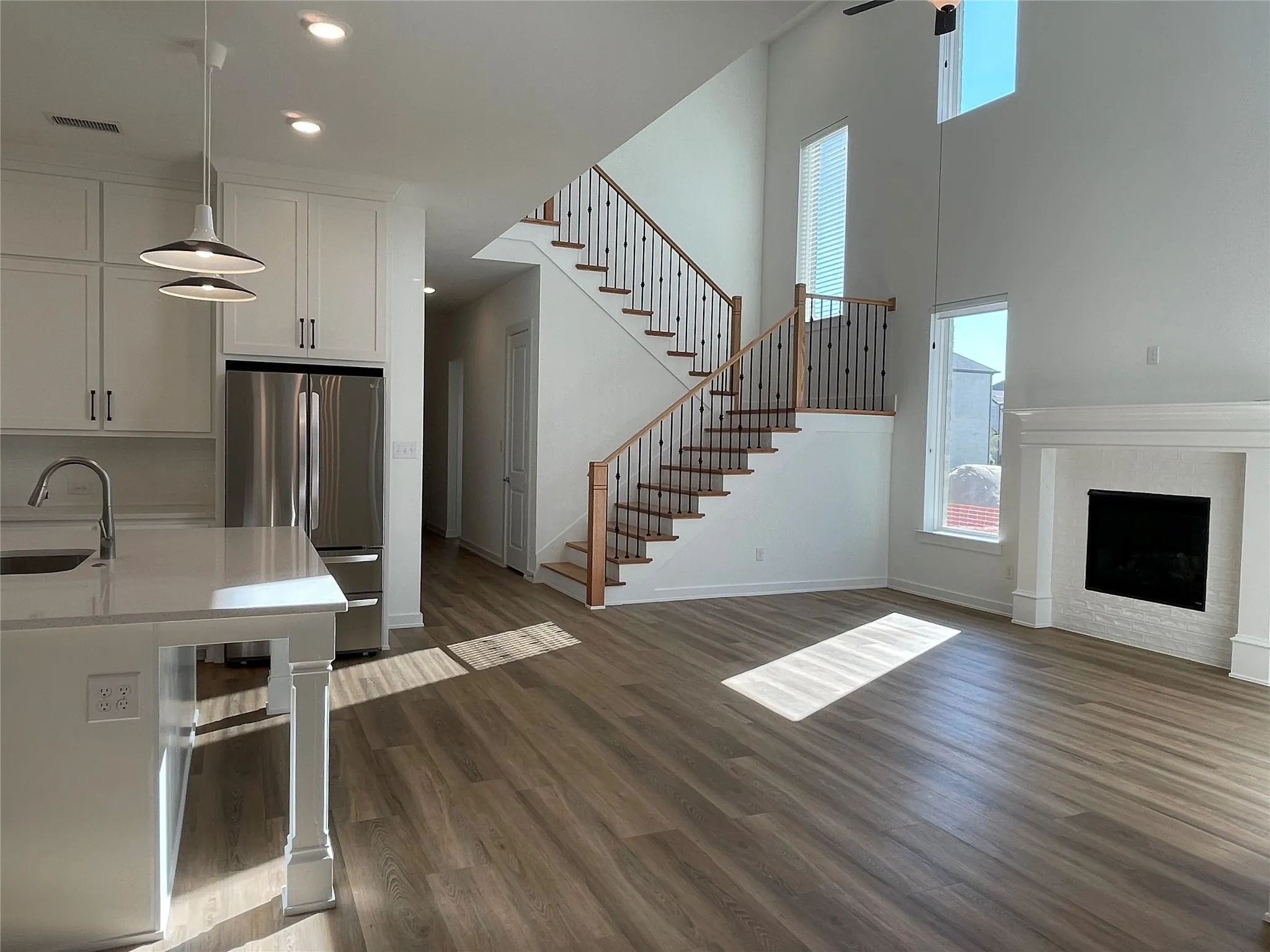 Open concept living area featuring wood-finish flooring, a white fireplace with mantle, and a grand staircase with wood treads and black iron balusters