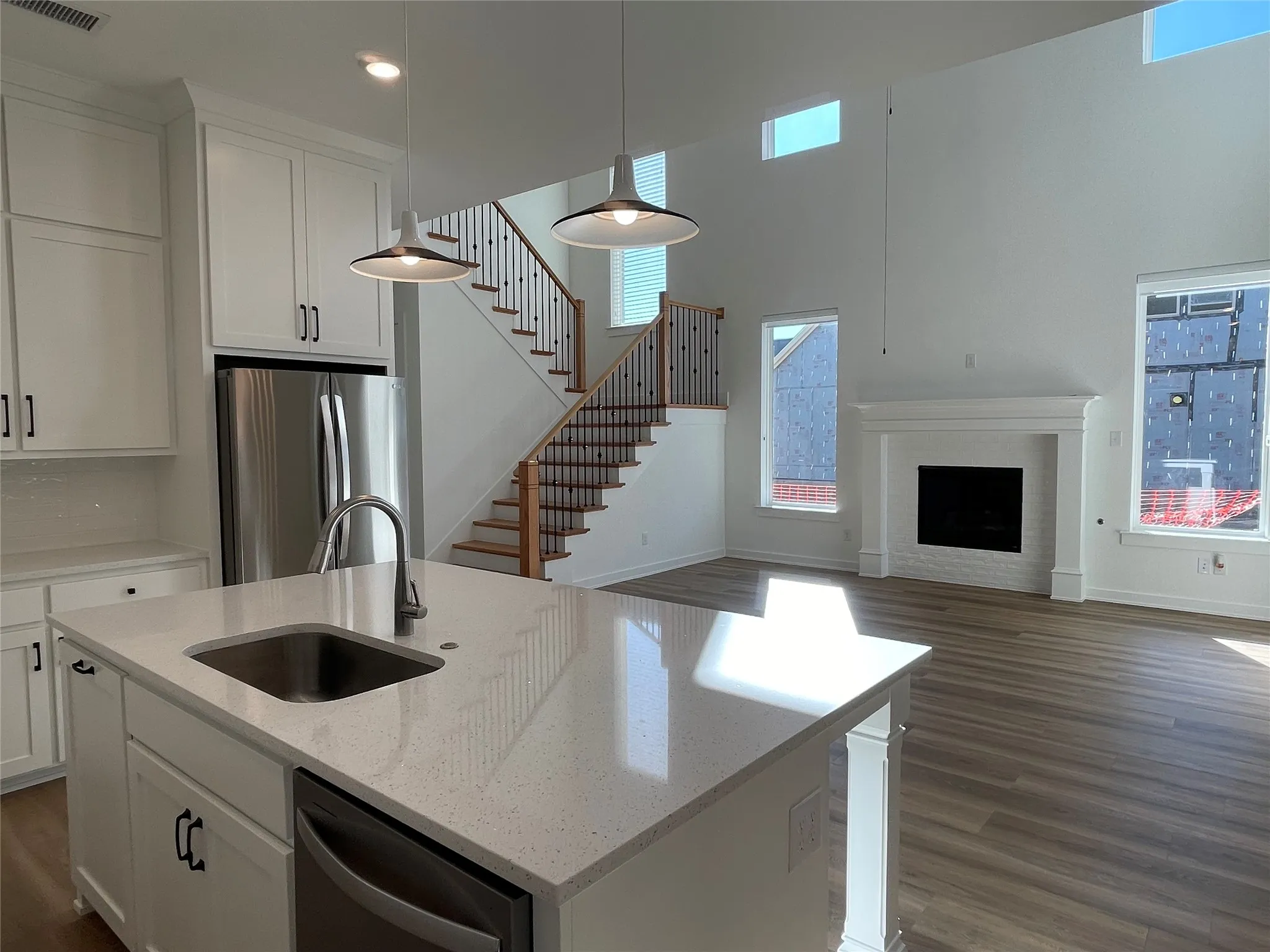 Open-concept living space featuring a kitchen island with an undermount sink, pendant lighting, stainless steel appliances, a fireplace with a white mantle, and wood-finish flooring