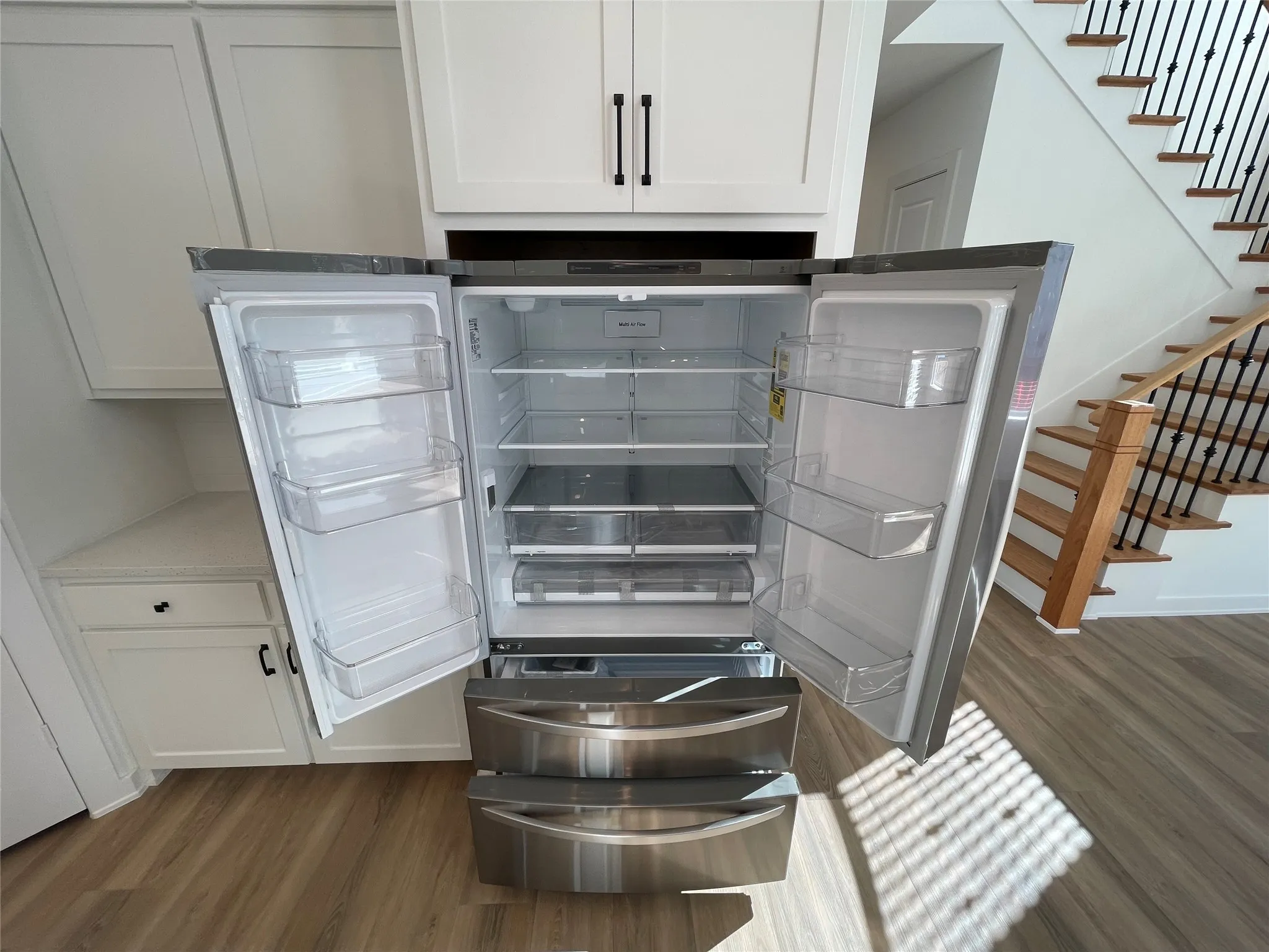 Stainless steel French door refrigerator with integrated cabinetry, wood-finish flooring, and a stairway featuring wood treads and wrought iron spindles