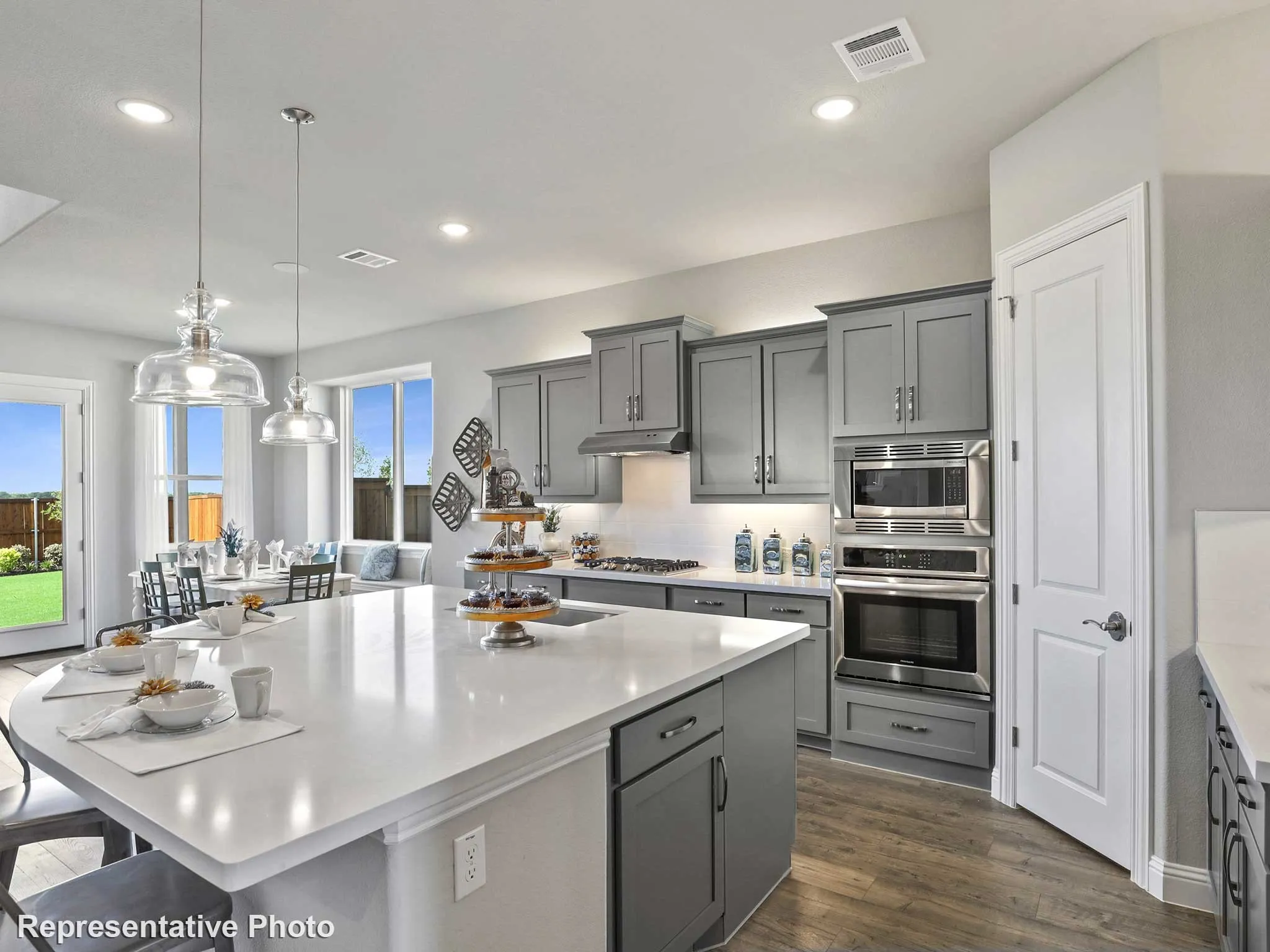 Contemporary kitchen featuring a large central island with a solid surface countertop, grey cabinetry, stainless steel appliances, and wood-finish flooring