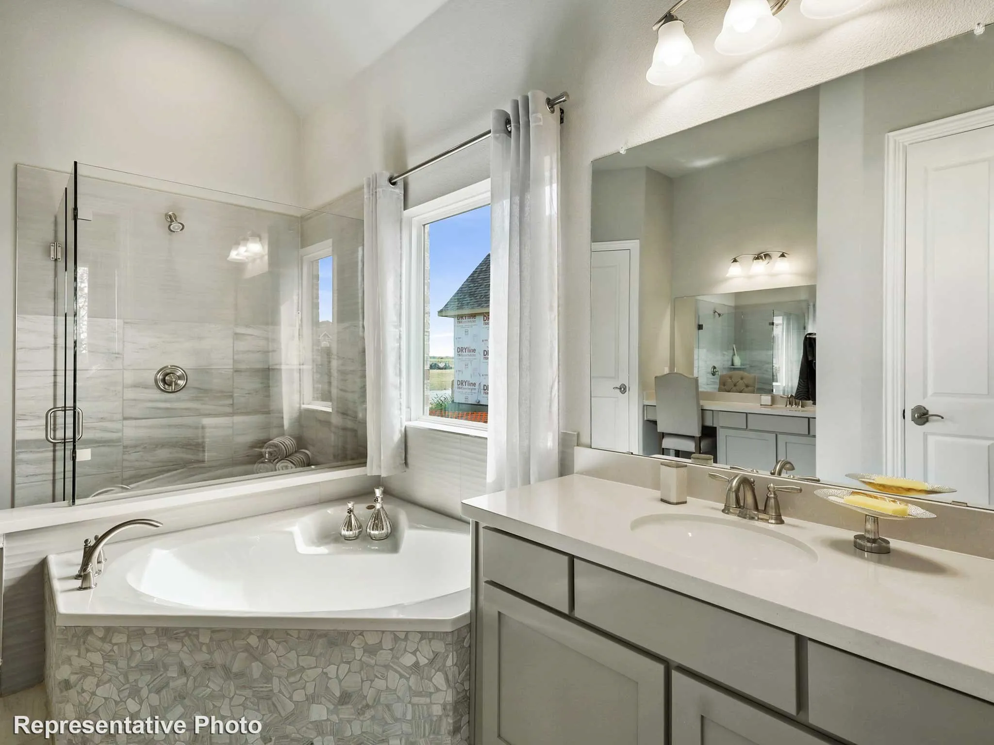 Bathroom featuring a corner soaking tub with pebble-tile surround, a glass-enclosed shower with tile walls, a vanity with a drop-in sink and ample counter space, and a separate vanity area