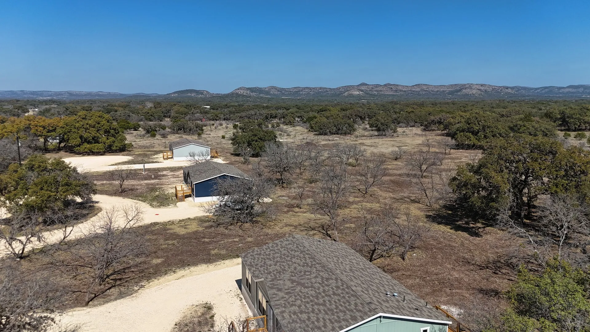 Expansive rural property featuring multiple structures, gravel driveways, and mature trees under a clear sky