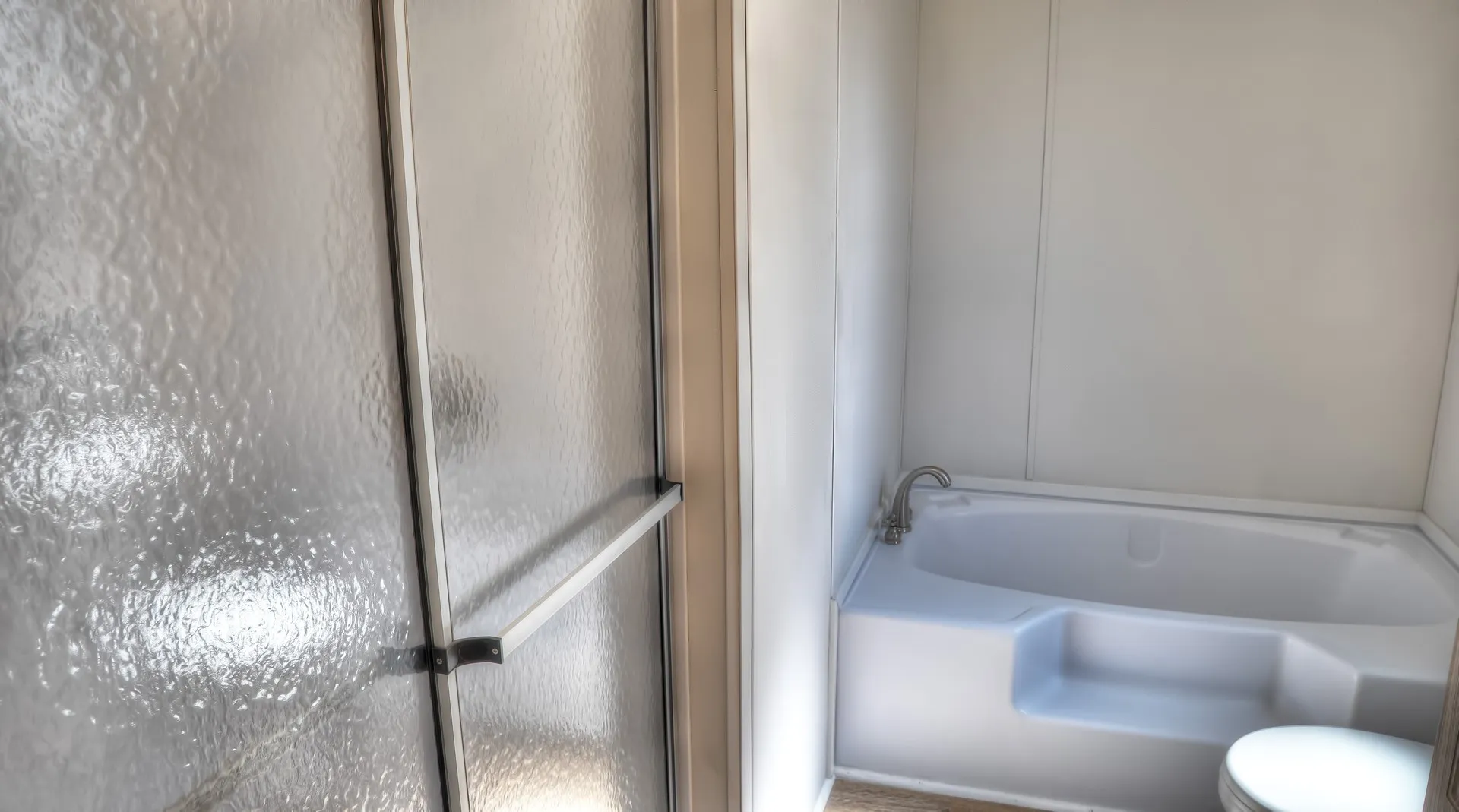 Bathroom featuring a white bathtub with integrated steps and a shower with frosted glass doors
