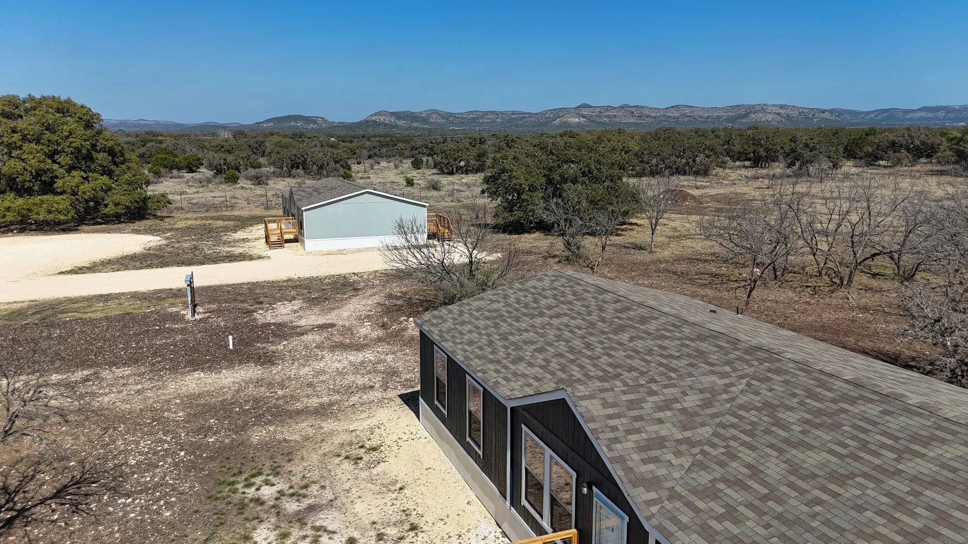 Contemporary residence with a multi-tone shingle roof and dark siding, complemented by a detached outbuilding featuring light blue siding