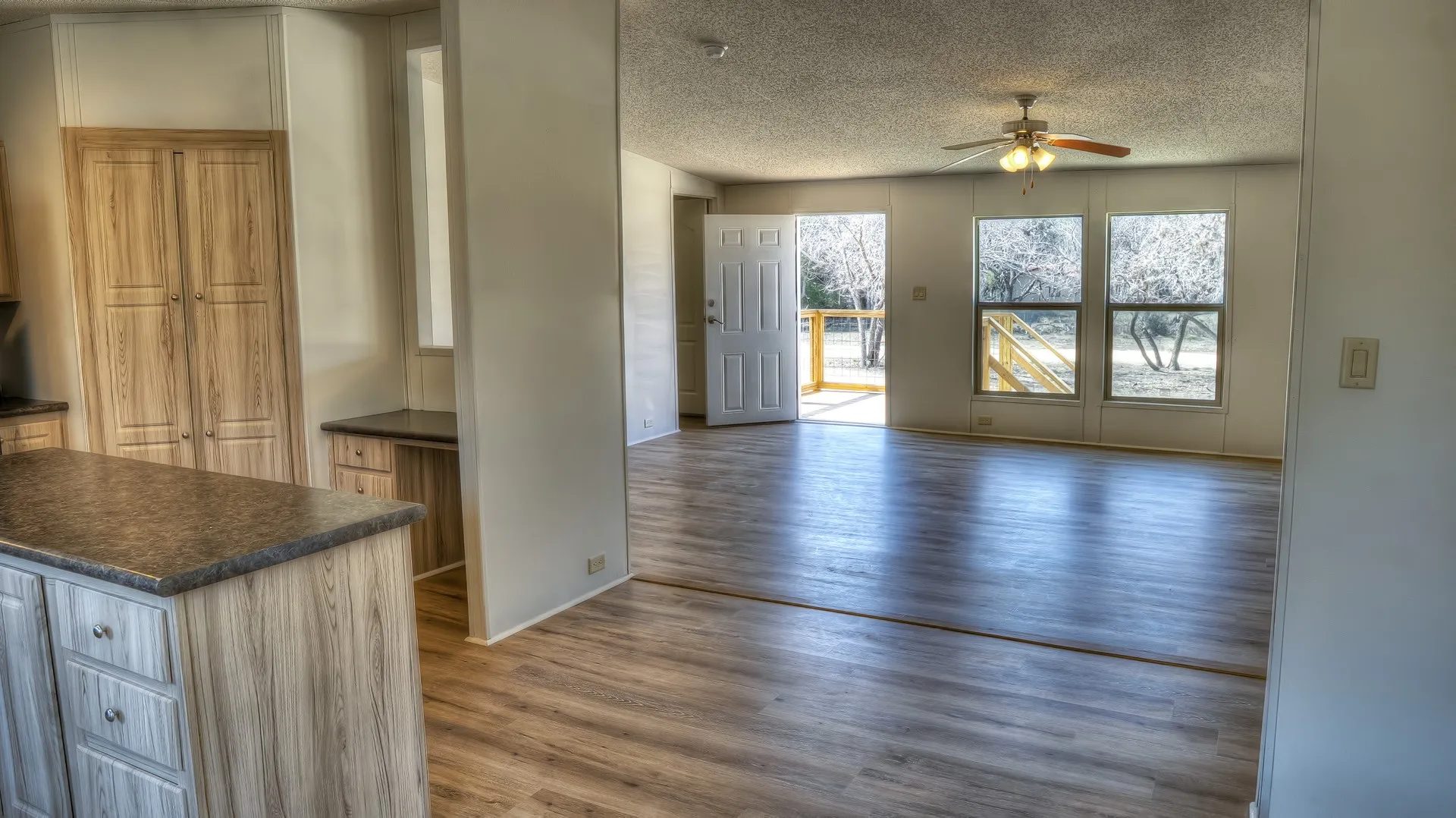 Open-concept living space with wood-finish flooring, a ceiling fan, and large windows