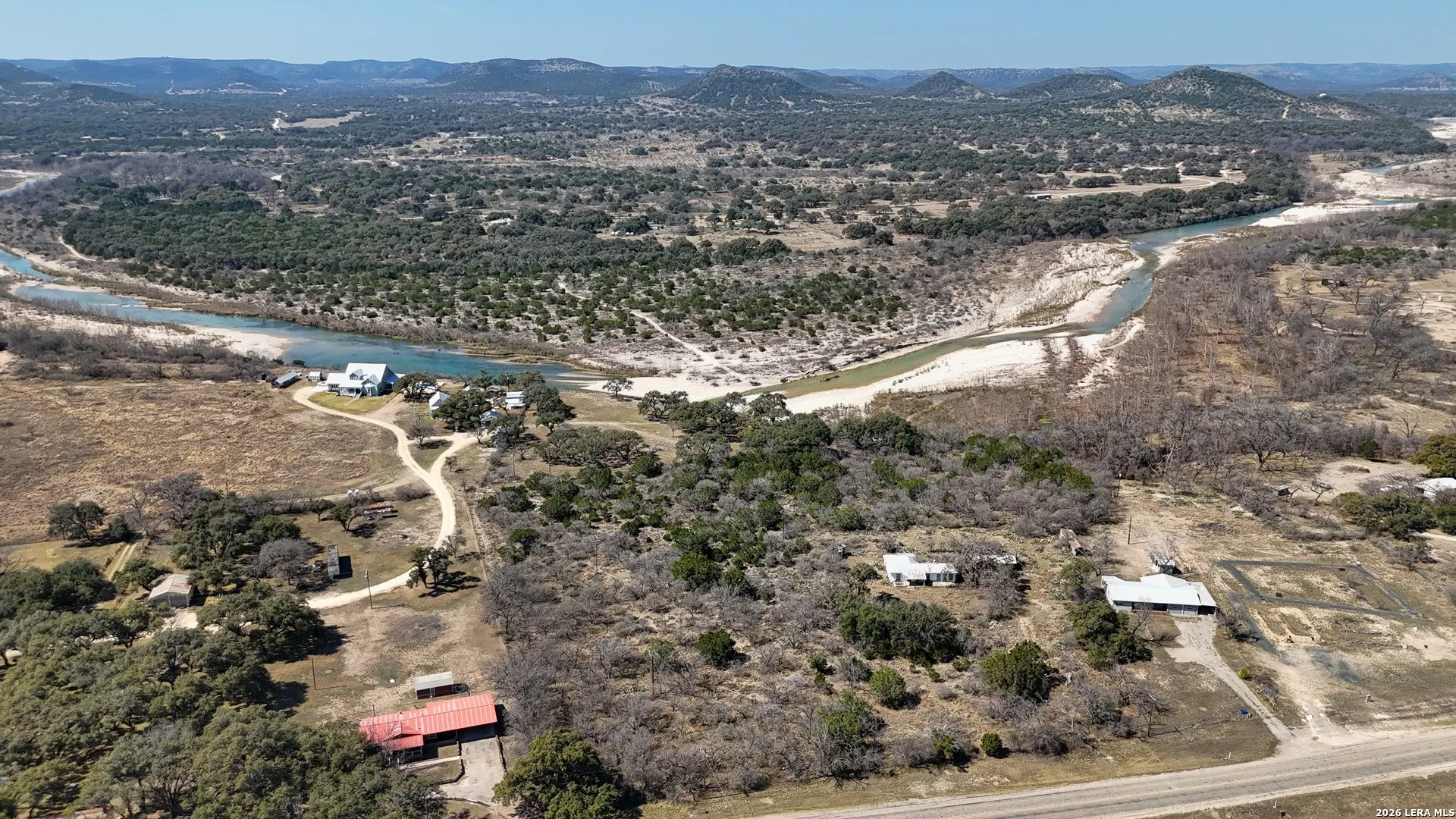 Expansive aerial landscape featuring a winding river, distant hills, natural vegetation, and multiple structures